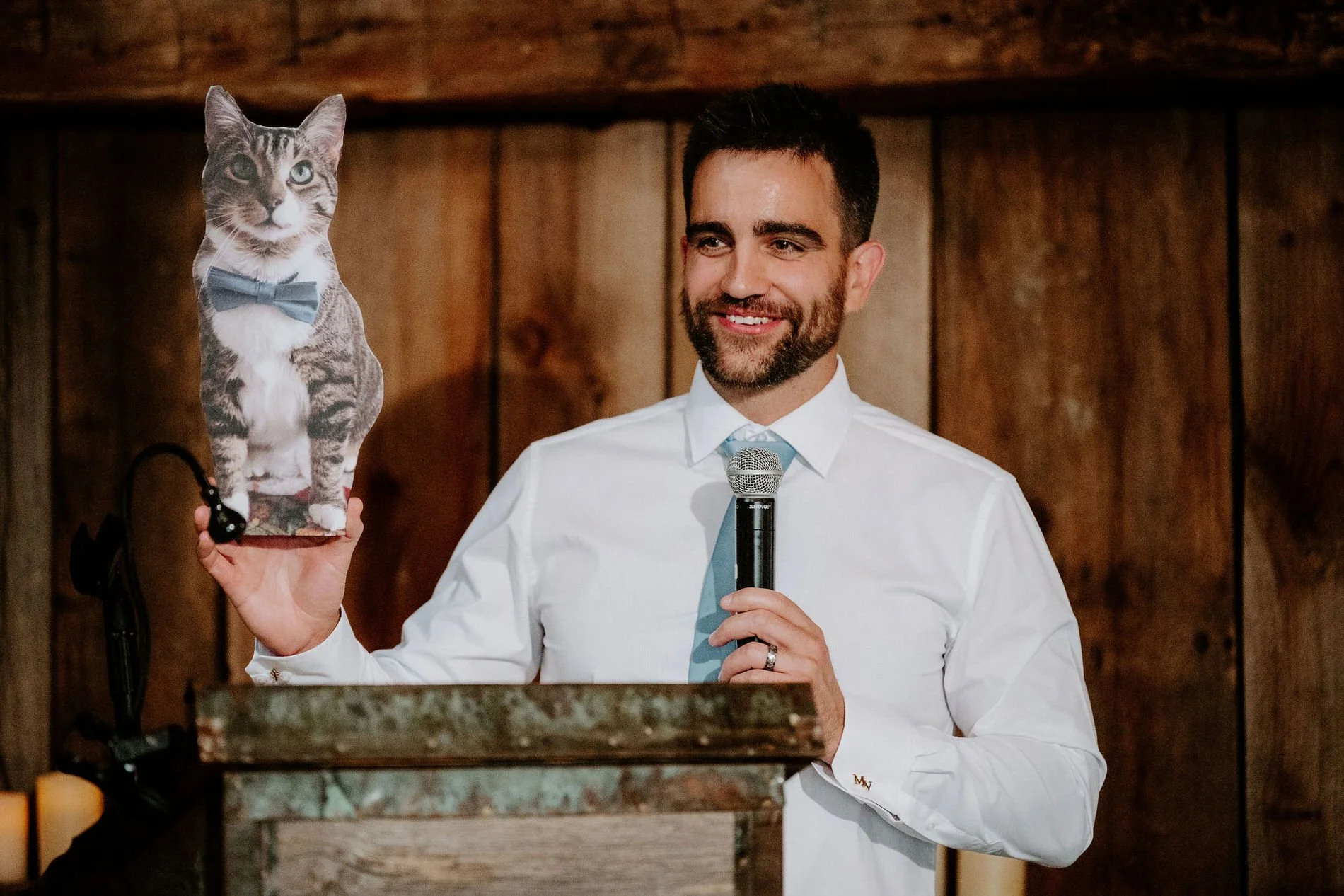 Man giving a speech while holding up a cardboard cutout of a tabby cat wearing a bow tie