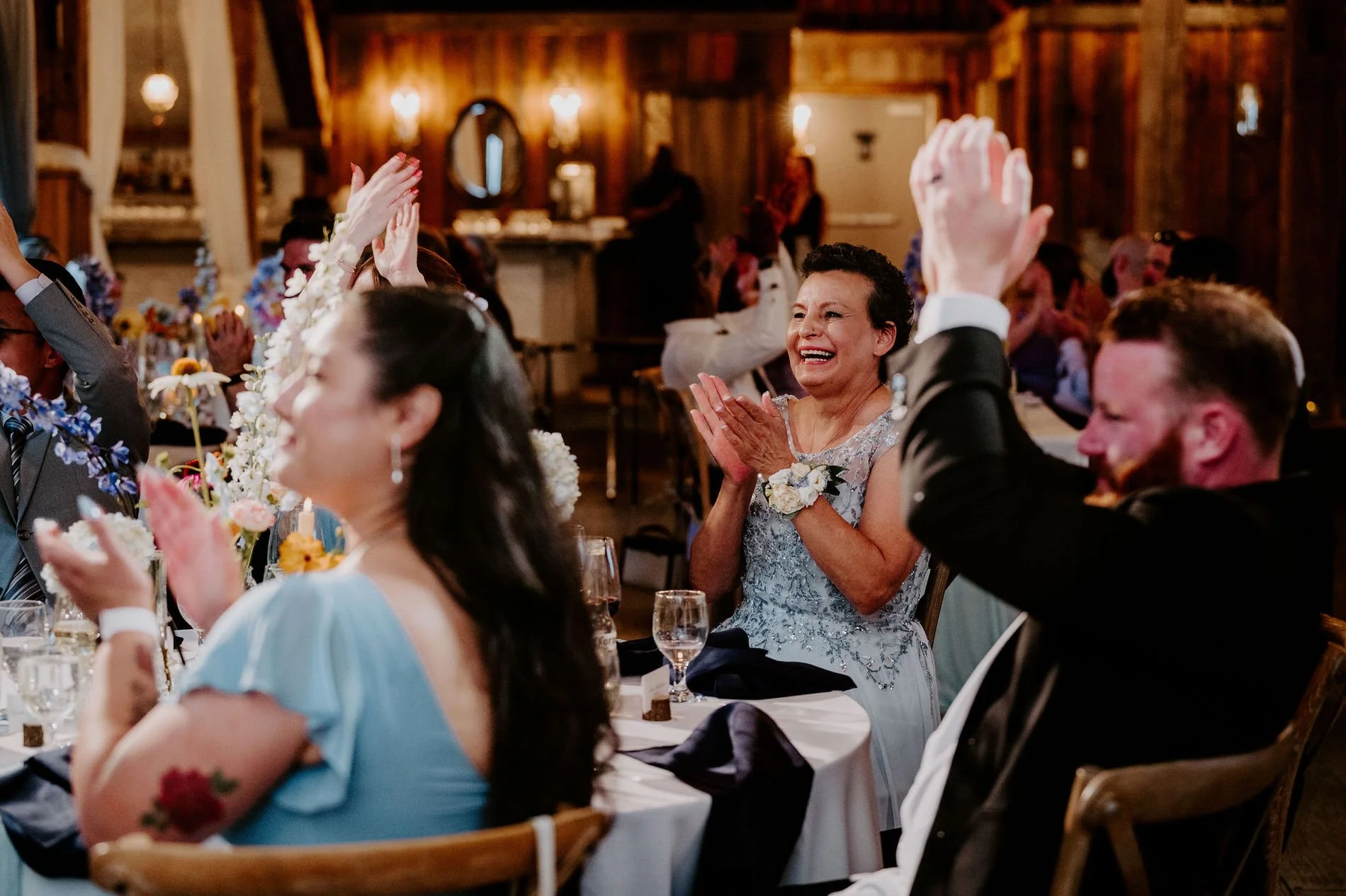 Guests applauding at Holly and Petar's reception, a woman in a blue lace dress beaming
