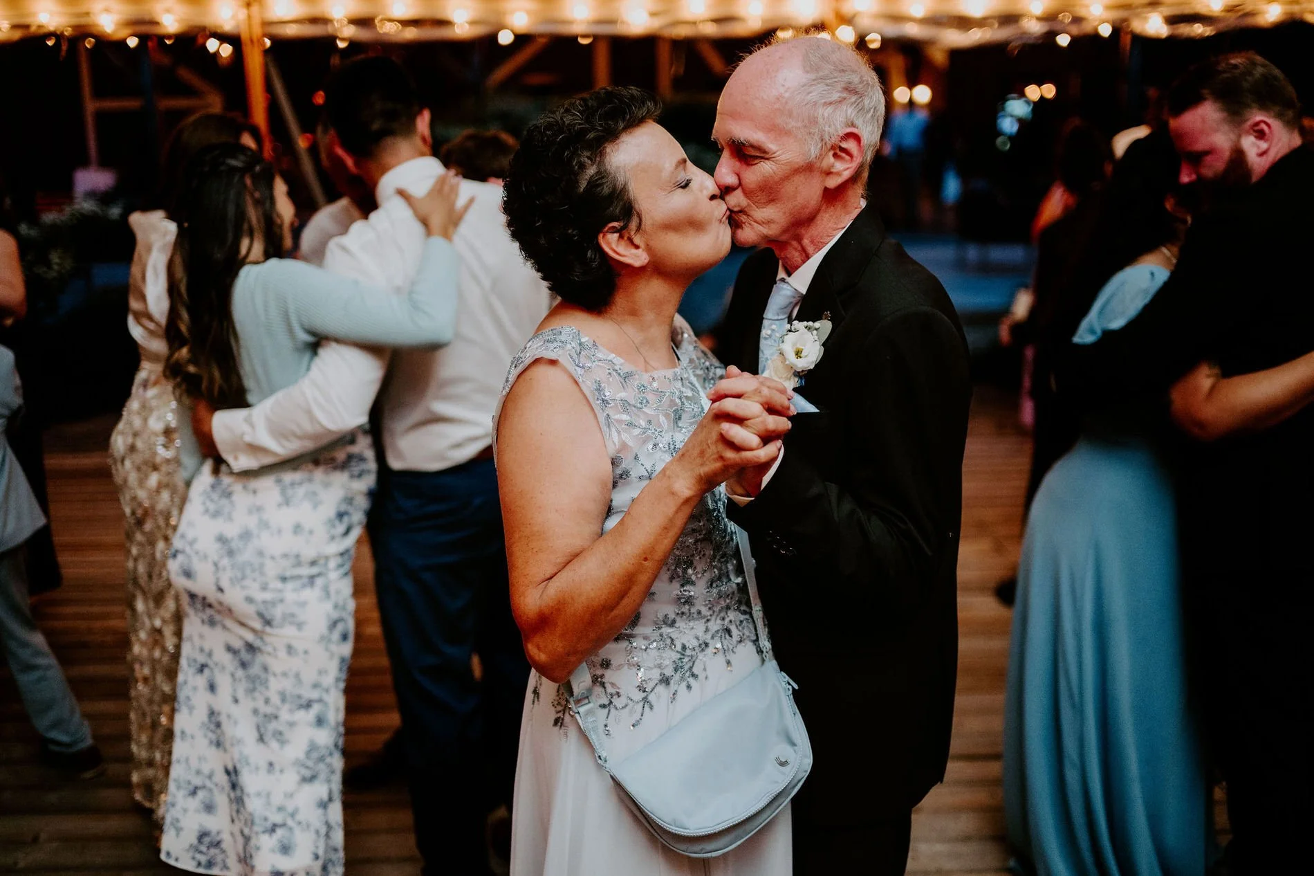 Holly's father sharing a kiss with a woman in a silver lace dress while slow dancing