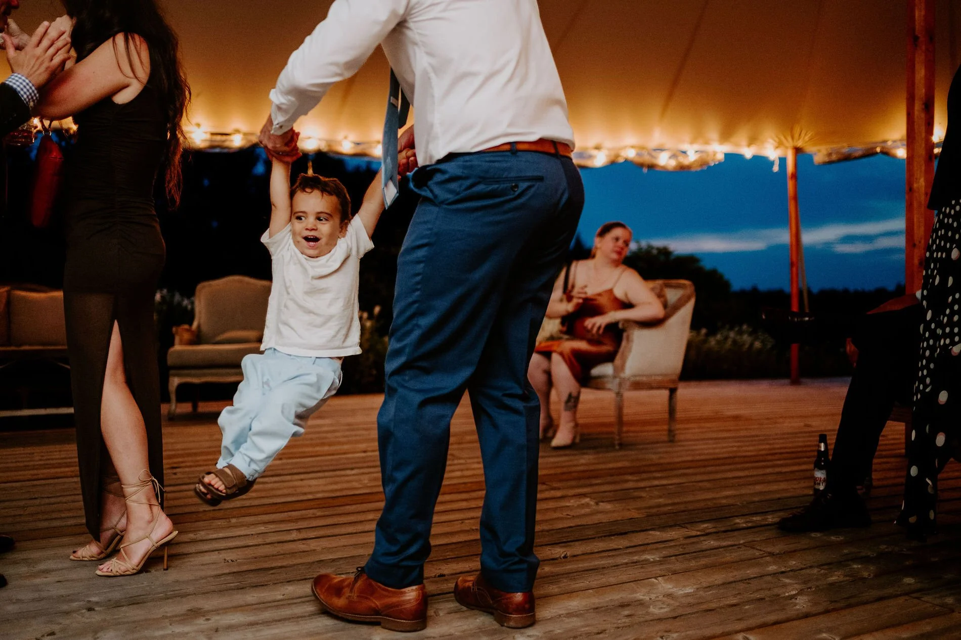 Man swinging a laughing toddler by the arms on the dance floor at Evermore at dusk
