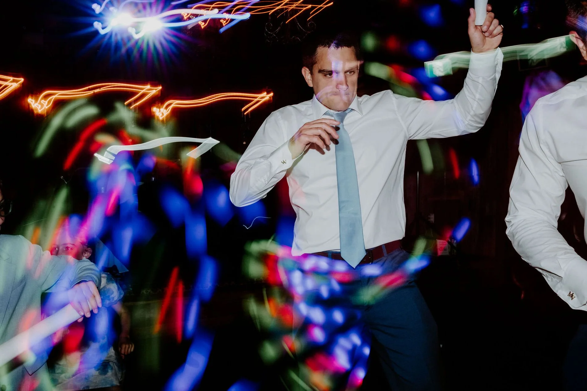 Guest dancing in a white shirt and pale blue tie, surrounded by streaks of coloured light