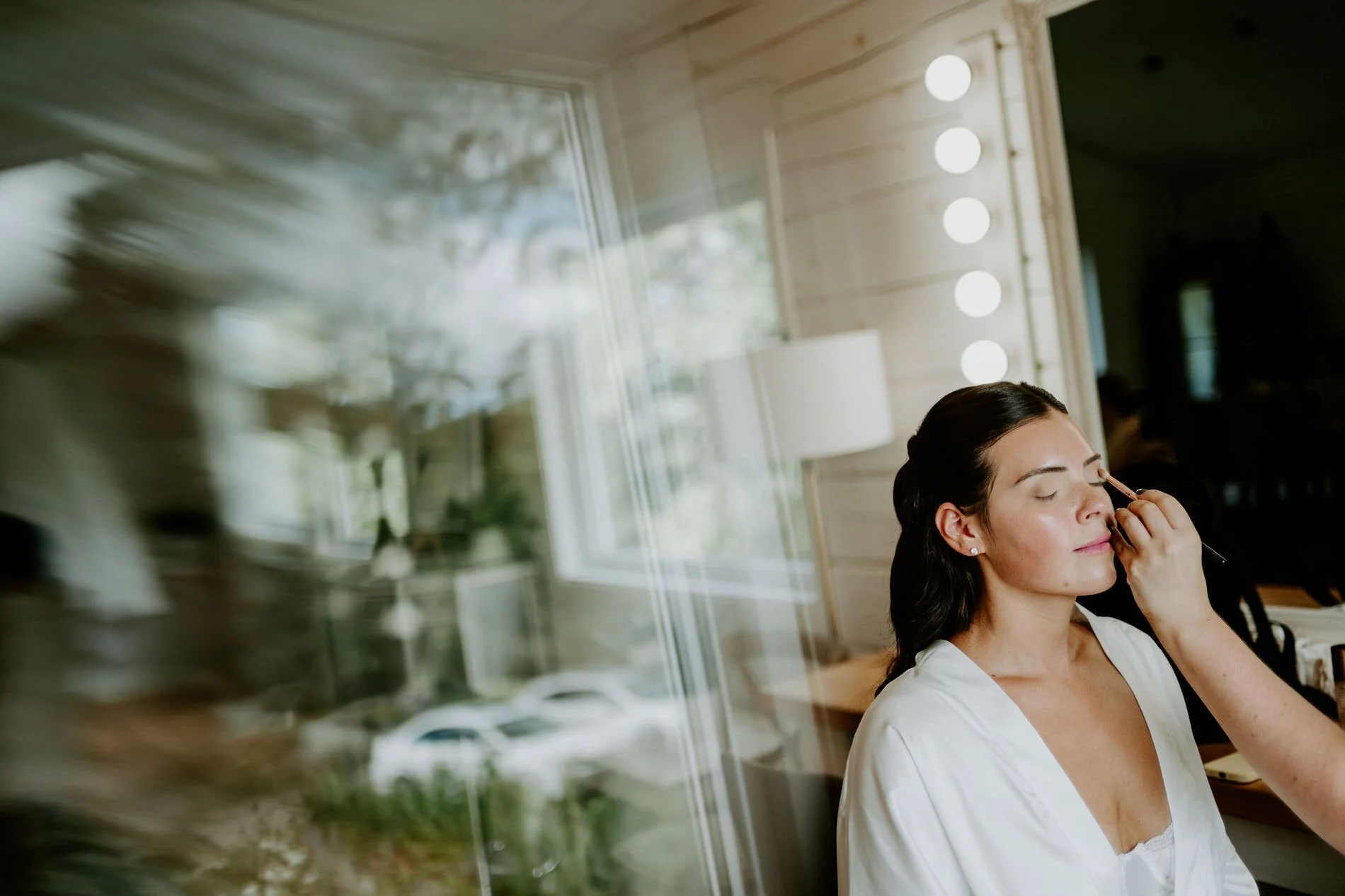 Kylie having her makeup done beside a sunny window on the morning of her Wakefield, Quebec wedding