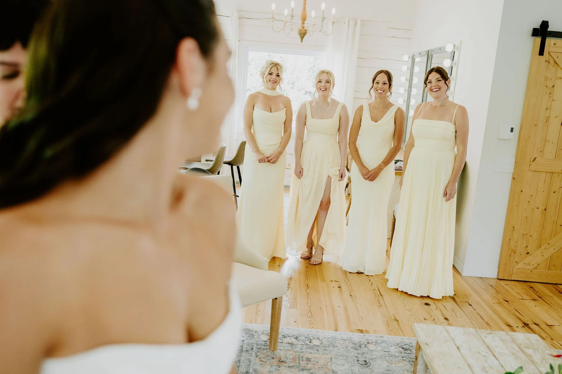 Bridesmaids in pale yellow gowns smiling as they see Kylie in her wedding dress for the first time