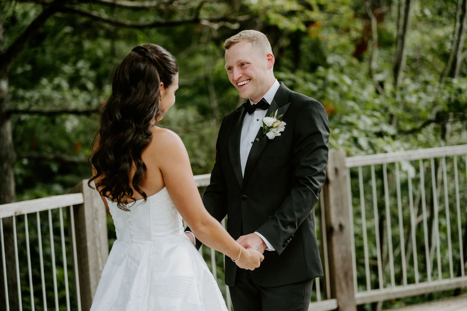 Kylie and Will holding hands during their first look on a wooden deck surrounded by trees at Le Belvedere