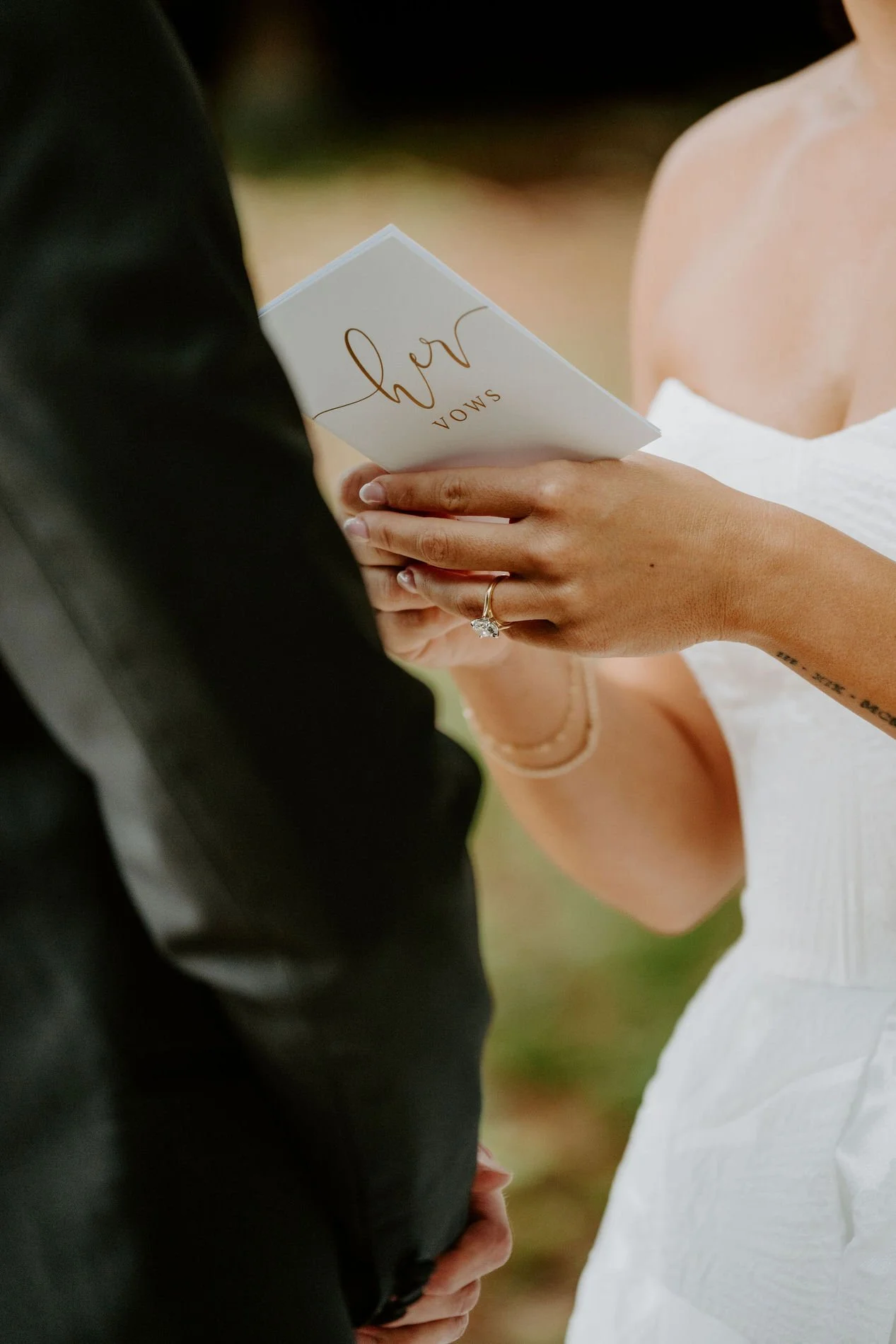 Close-up of Kylie holding a card reading "her vows" in gold script