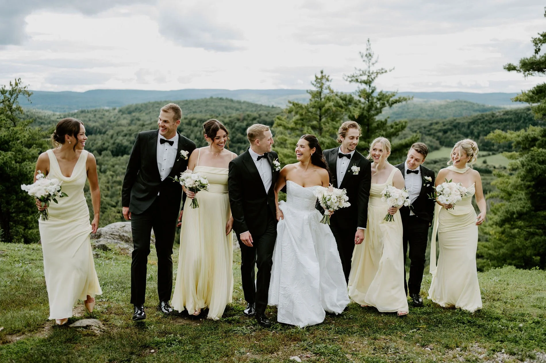 Kylie and Will's wedding party walking across a hilltop at Le Belvedere, with the Gatineau Hills behind them