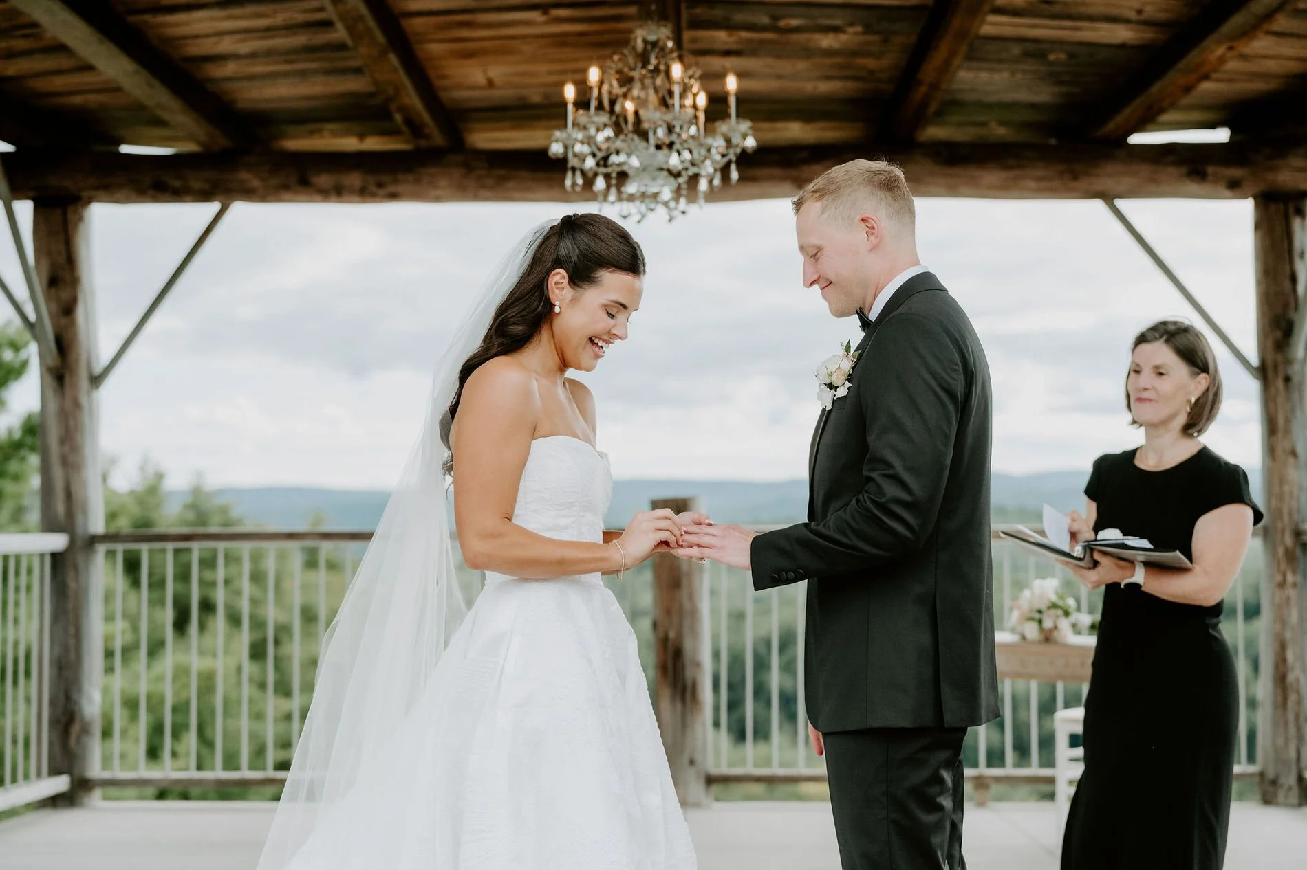 Kylie laughing as Will slides on her wedding ring under the chandelier at Le Belvedere