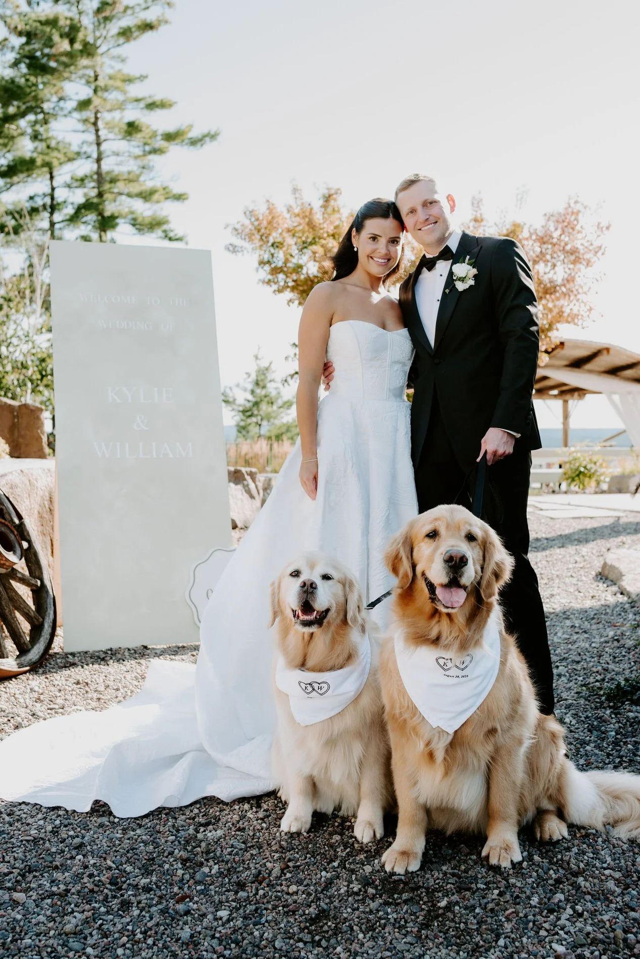 Kylie and Will with their two golden retrievers beside a "Kylie &amp; William" welcome sign at Le Belvedere
