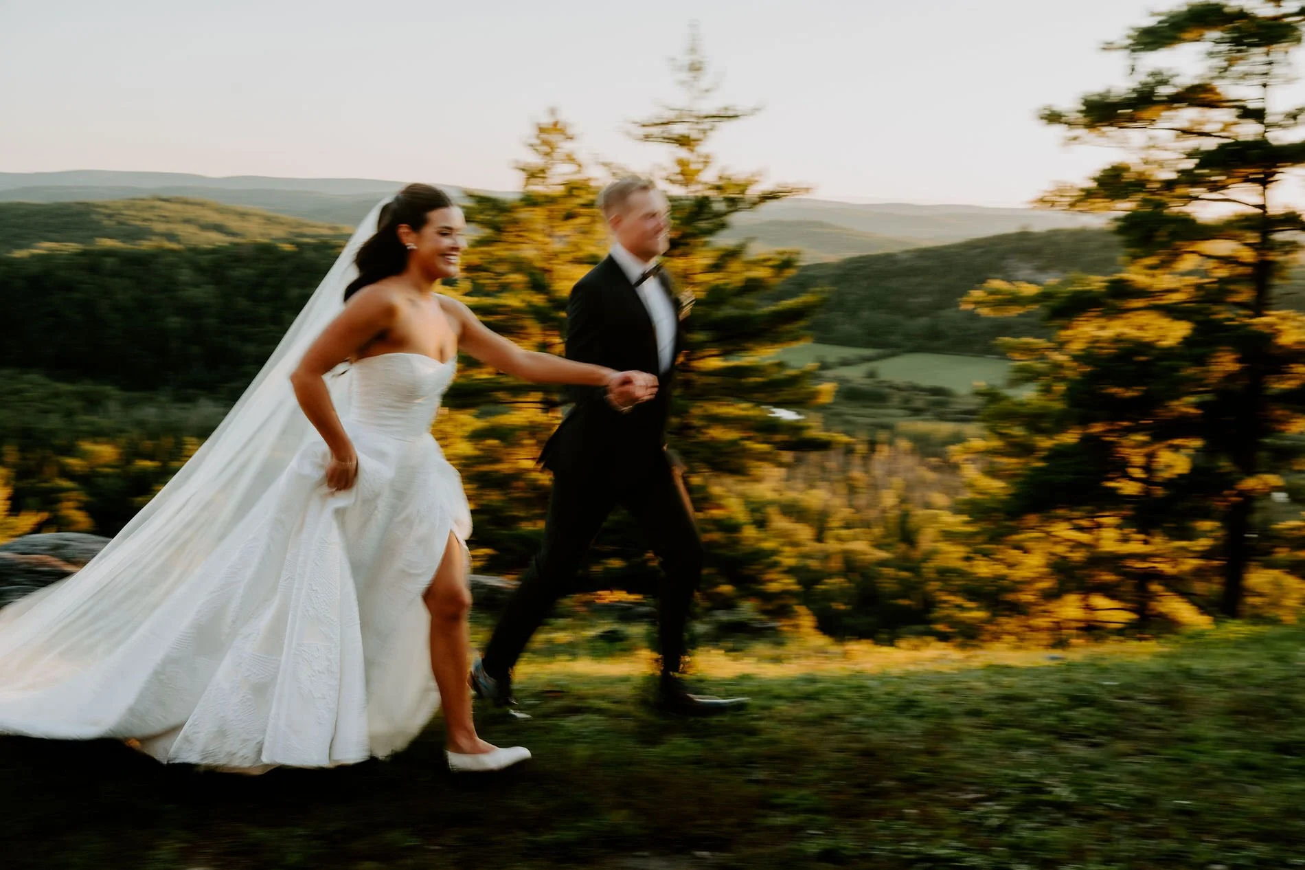 Kylie and Will running hand in hand across a hilltop at sunset, her veil trailing behind