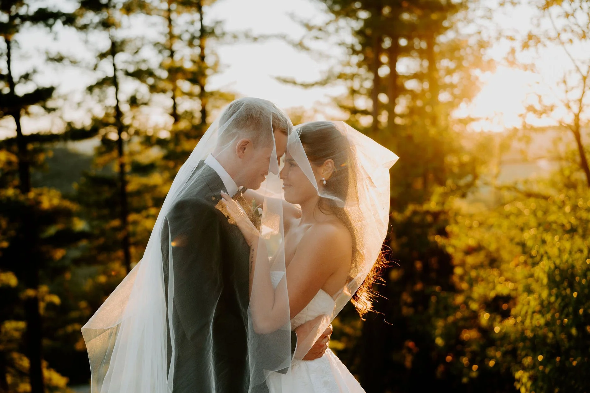 Kylie and Will nose to nose under her veil, backlit by the golden sunset