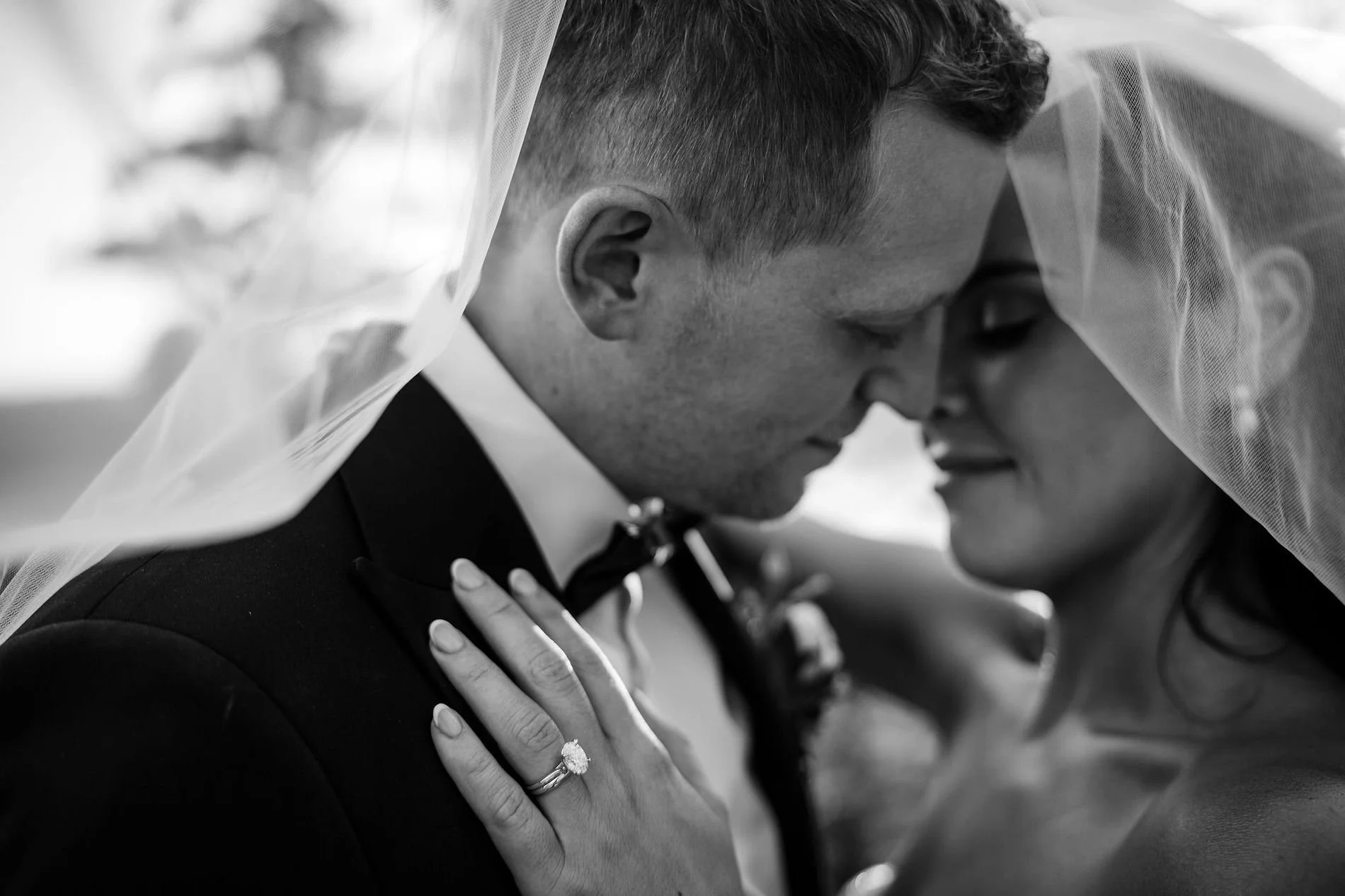 Black and white close-up of Kylie and Will under her veil, her engagement ring resting on his lapel