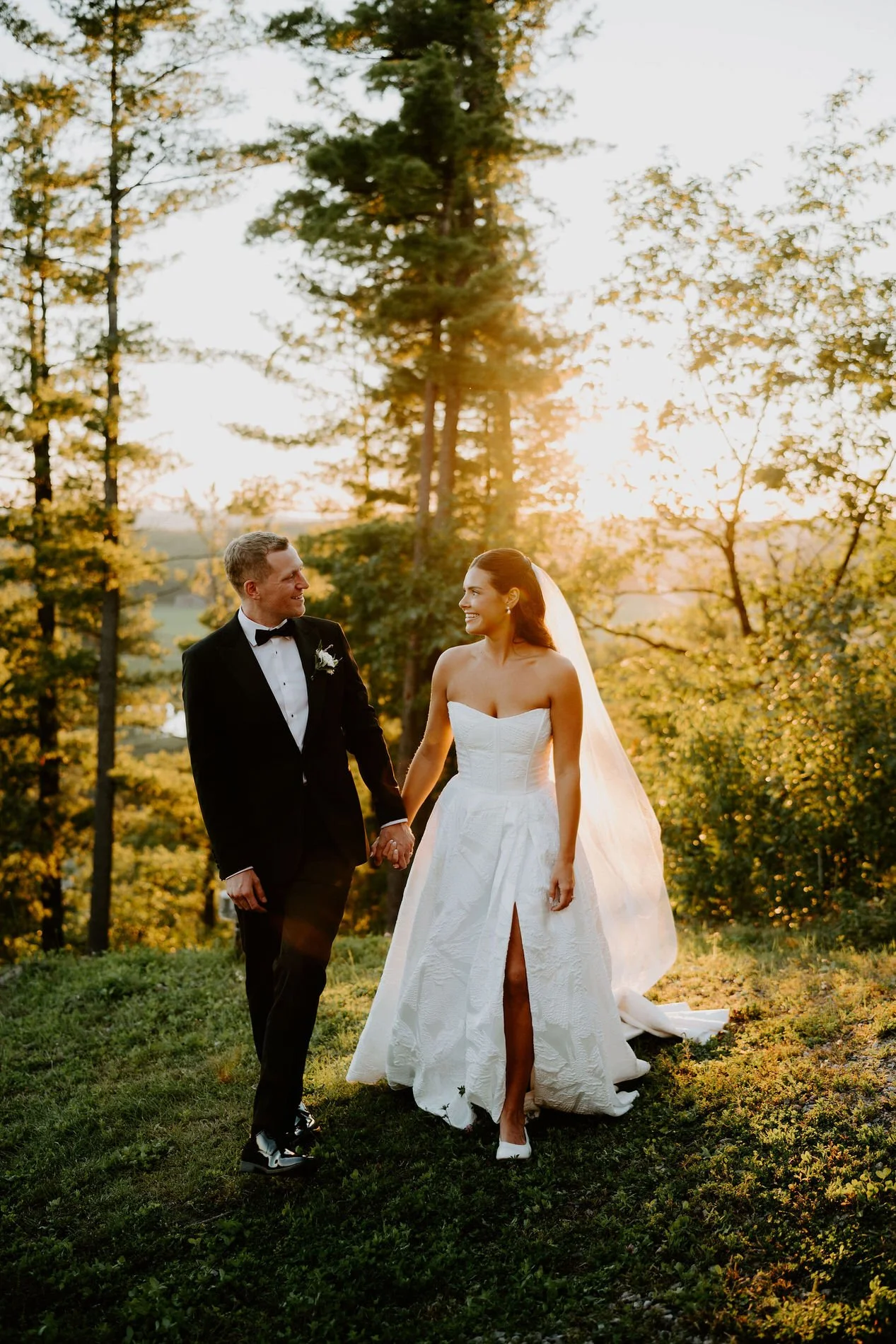 Kylie and Will walking hand in hand across the grass at sunset at Le Belvedere