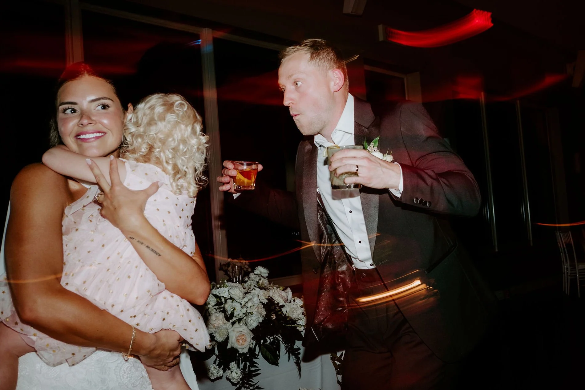 Will dancing with a drink in each hand beside Kylie, who holds a curly-haired toddler