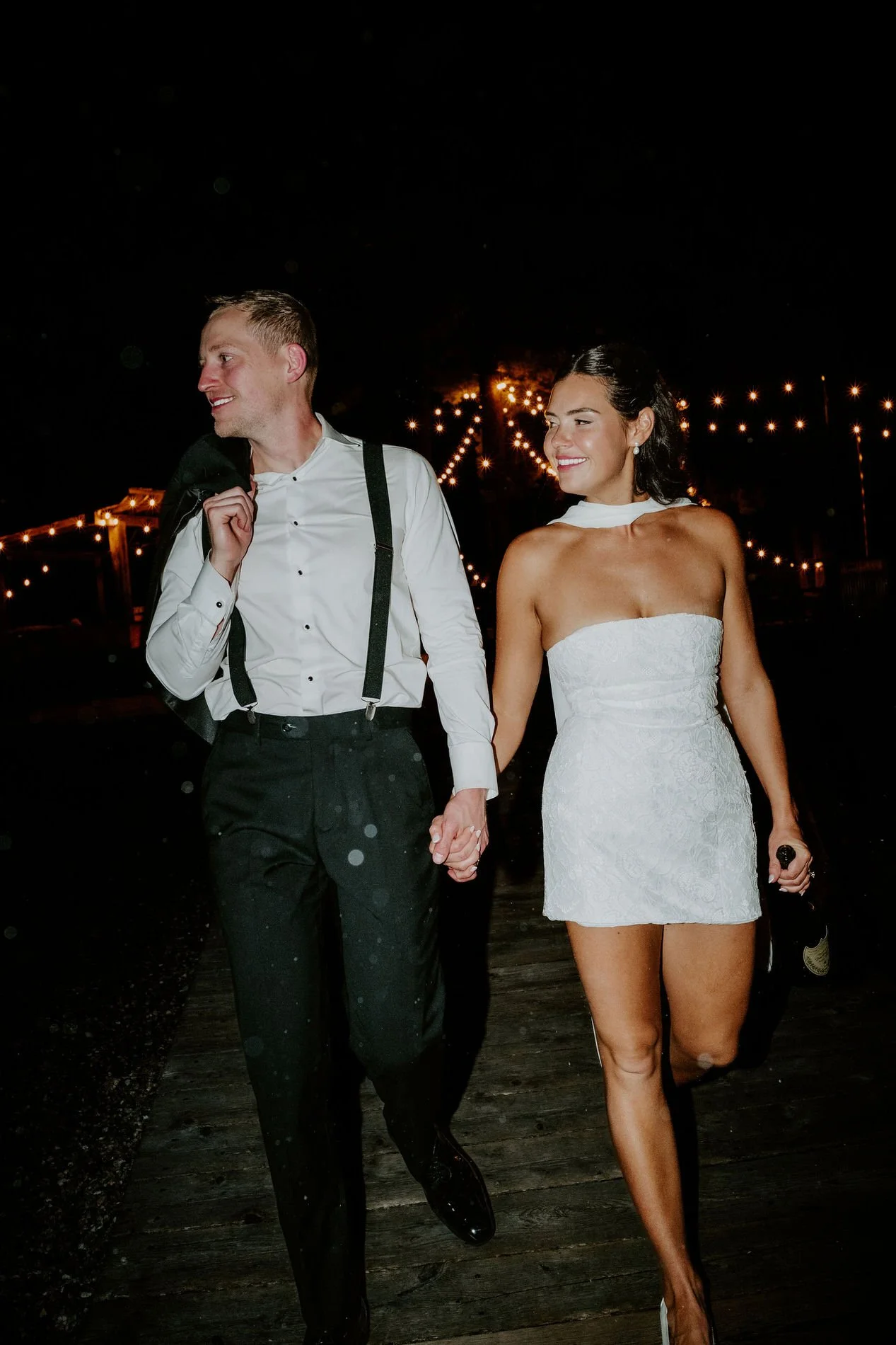 Kylie in a short white after-party dress walking hand in hand with Will under string lights