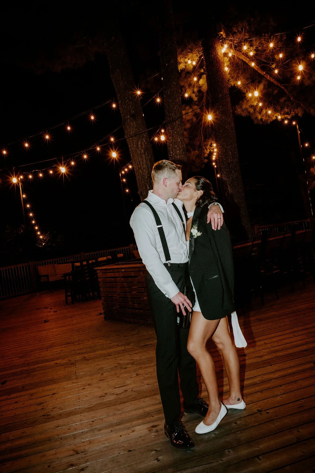 Kylie and Will kissing under string lights on the deck at Le Belvedere at the end of the night