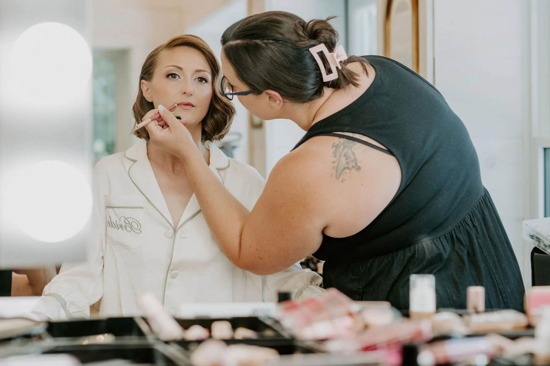 A makeup artist applying lipstick to Emily, who wears a "Bride" pyjama top, on the morning of her Stonefields Estate wedding