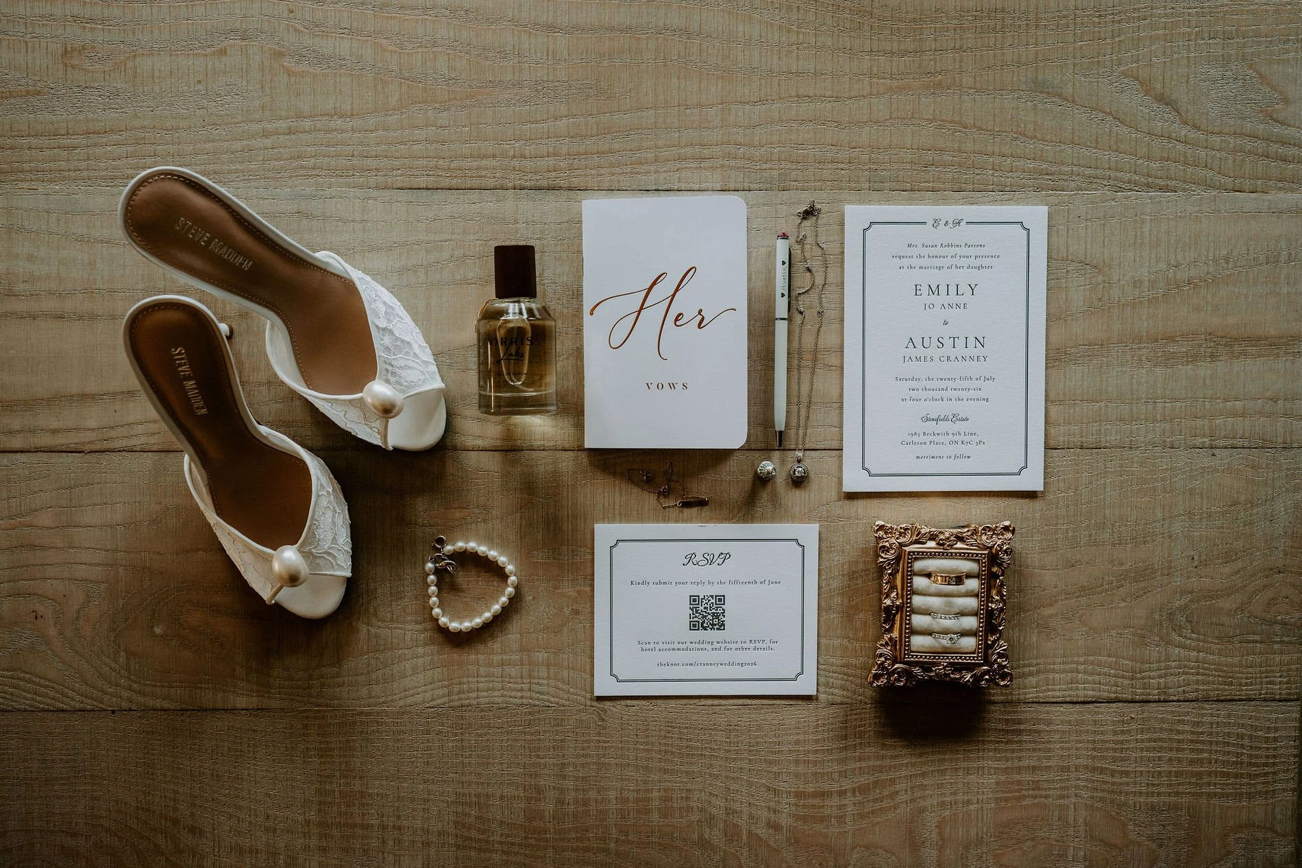 Flat lay of Emily's pearl-trimmed heels, perfume, "Her Vows" booklet, Emily and Austin's invitation and a gilded ring box