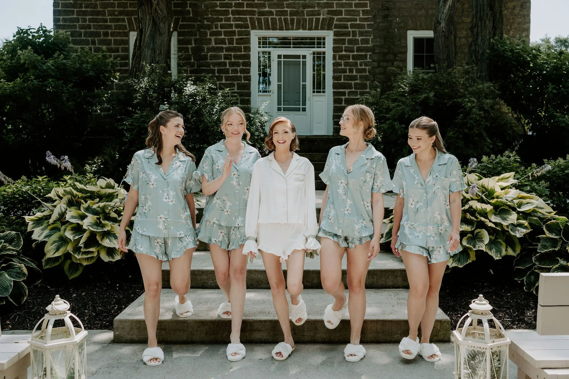 Emily and her bridesmaids in pyjamas and fluffy slippers on the steps of the stone house at Stonefields Estate