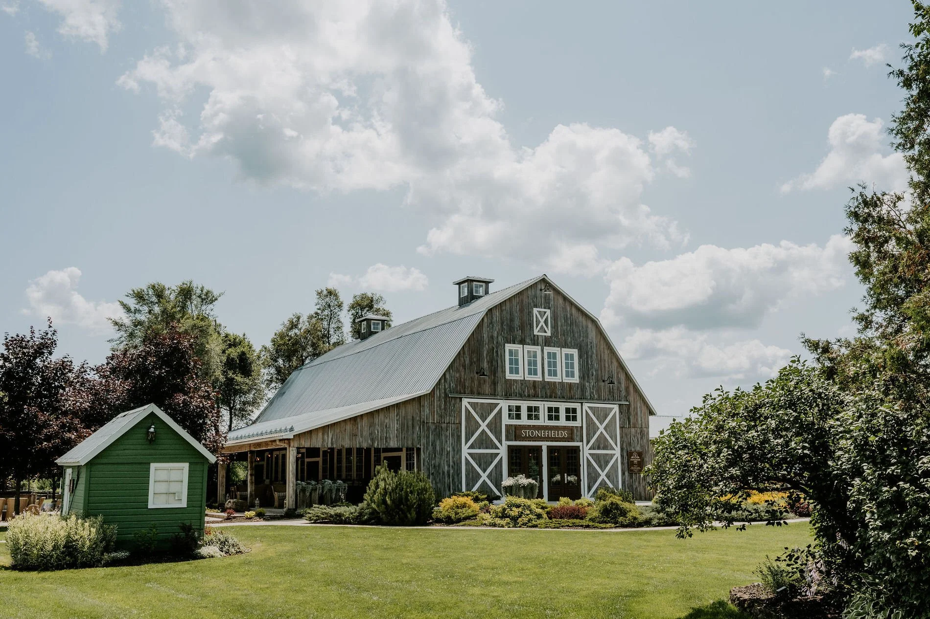 The weathered grey barn at Stonefields Estate near Ottawa, with white cross-braced doors and summer gardens