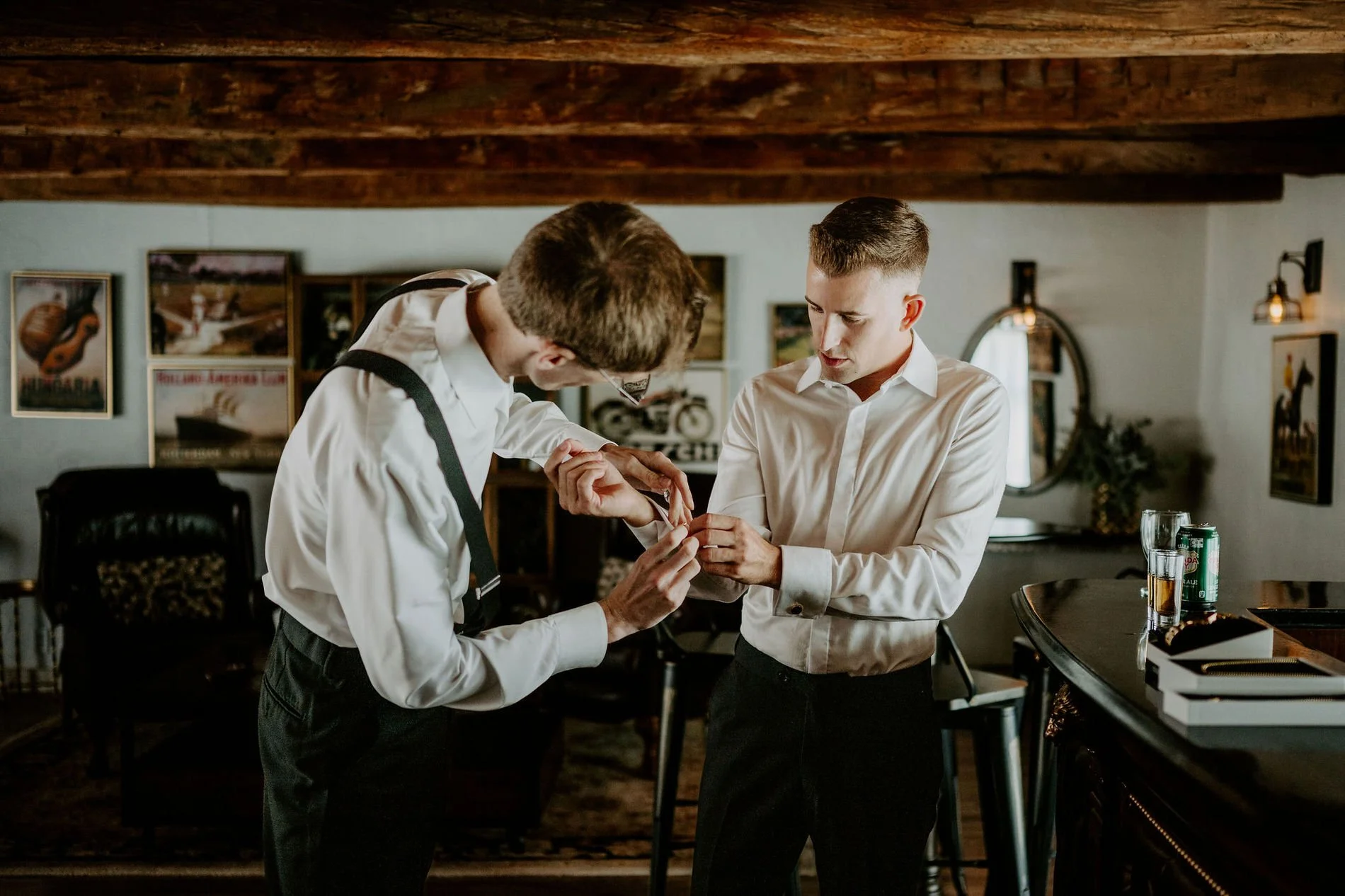 A groomsman helping Austin with his cufflinks beneath rustic wooden beams