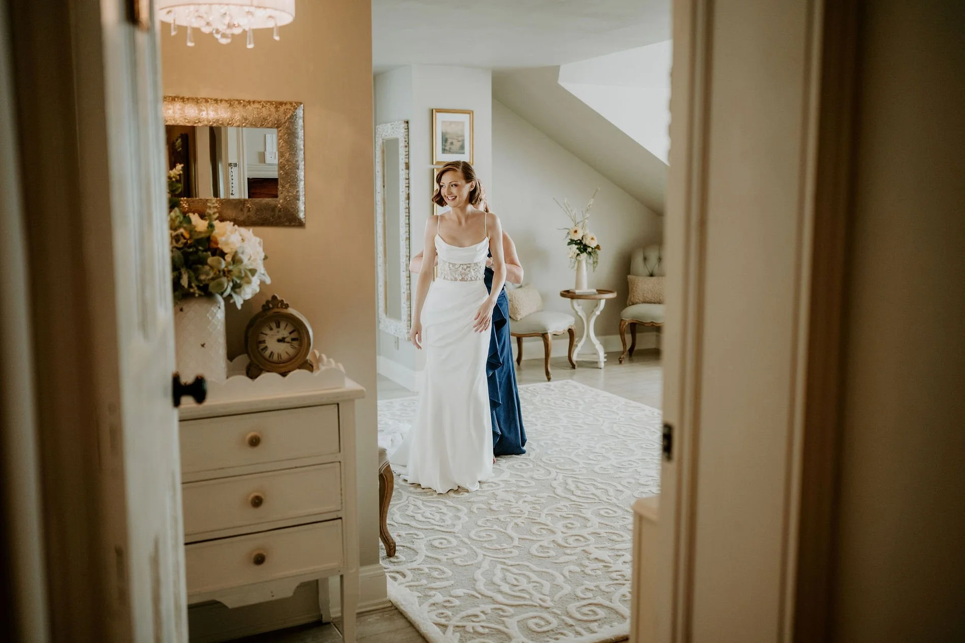 Emily in her gown seen through a doorway of the bright bridal suite at Stonefields Estate