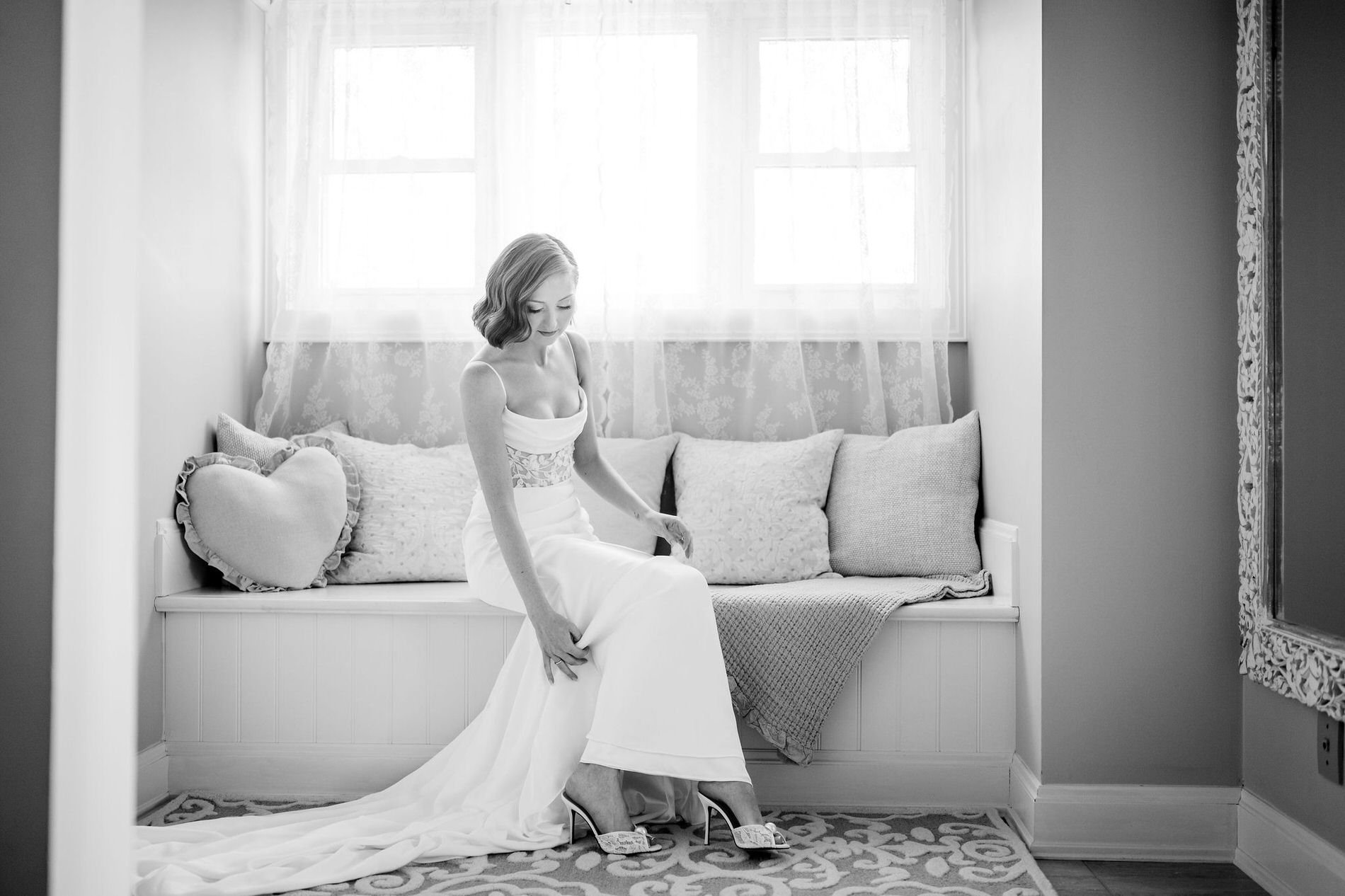 Black and white photo of Emily slipping on her heels on a window seat