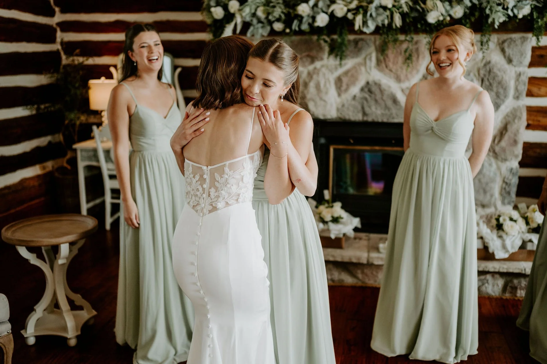Emily hugging a bridesmaid in front of the garland-draped stone fireplace
