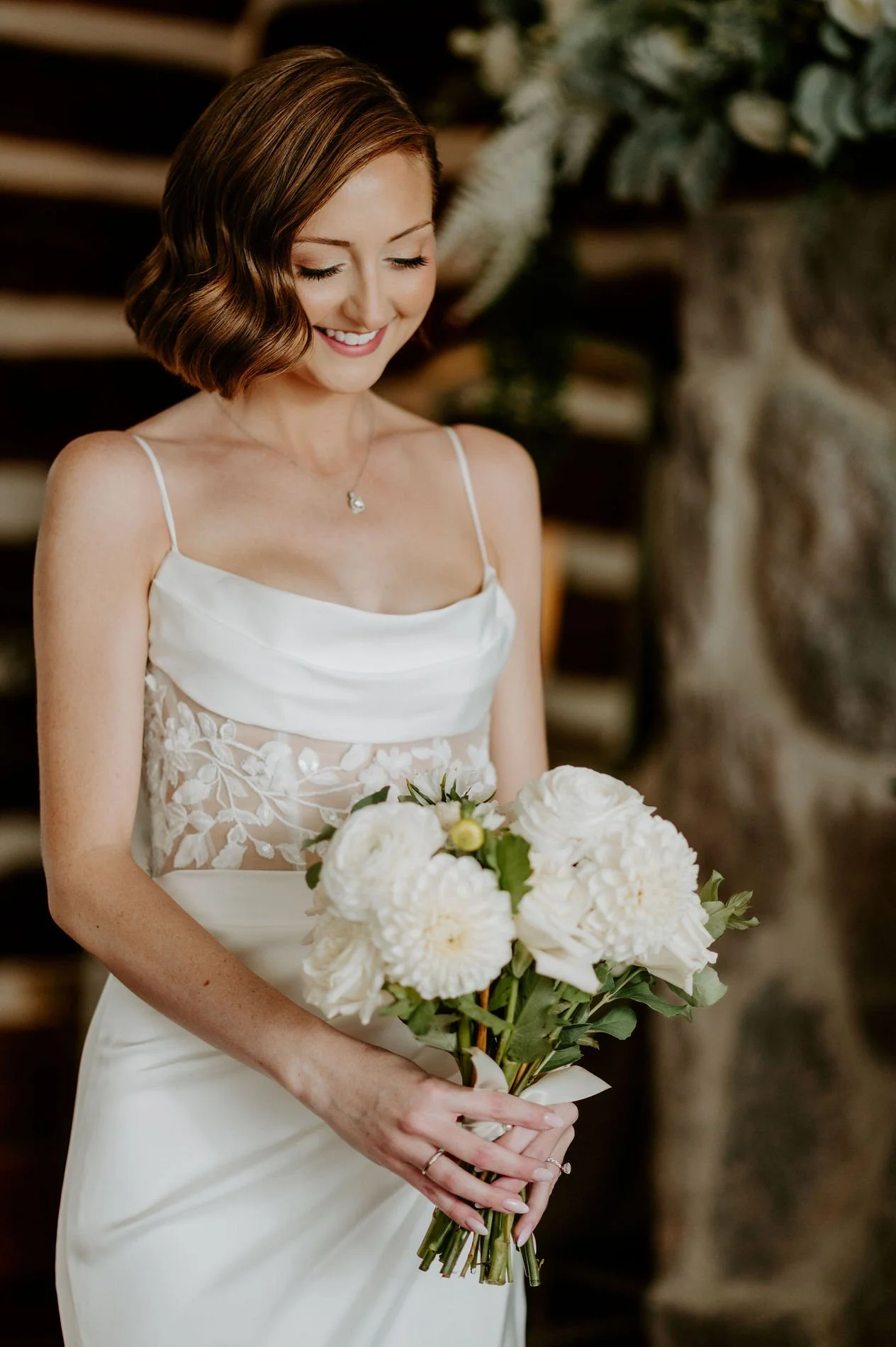 Emily smiling down at her bouquet of white dahlias and roses