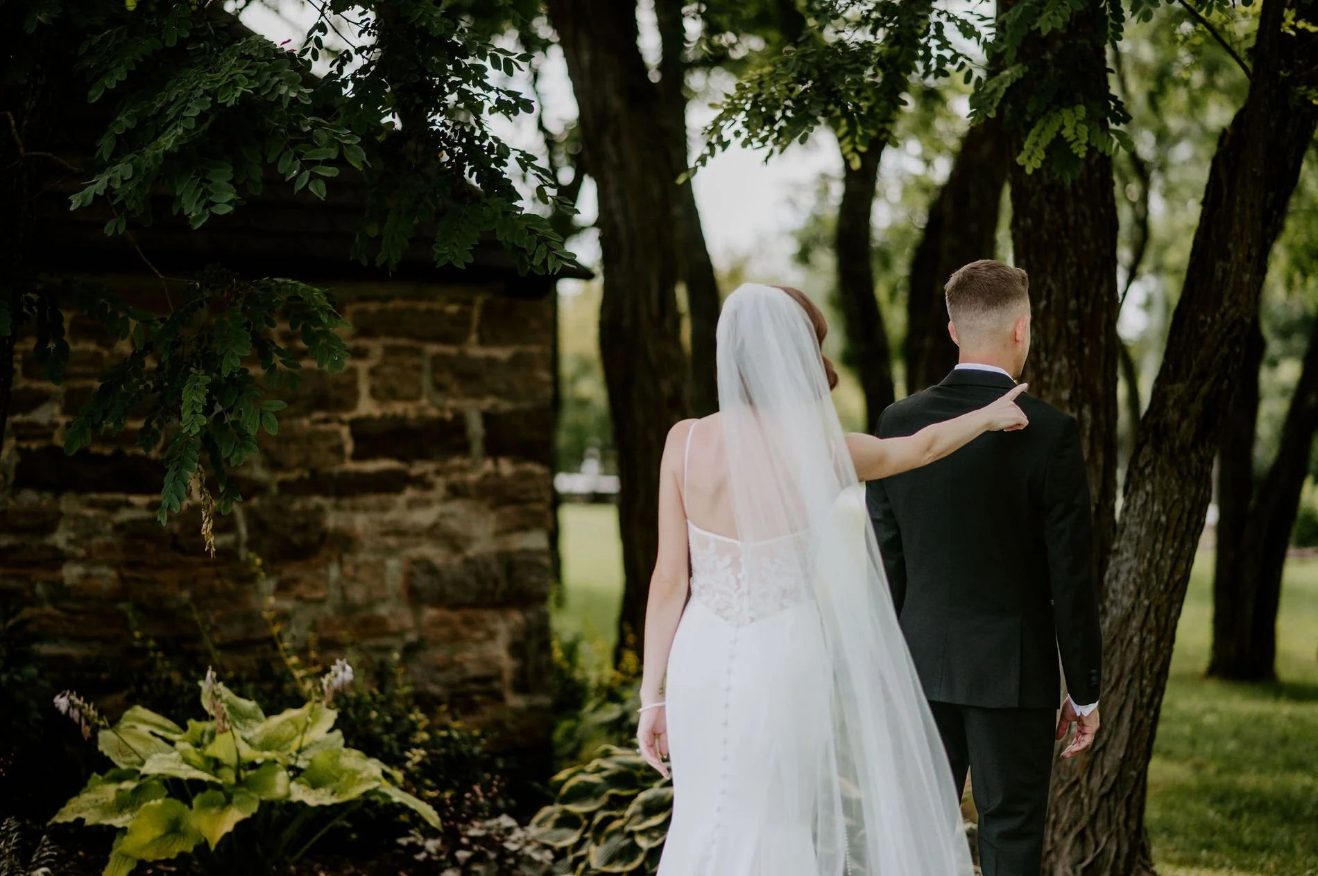 Emily tapping Austin on the shoulder for their first look beside a stone building at Stonefields Estate