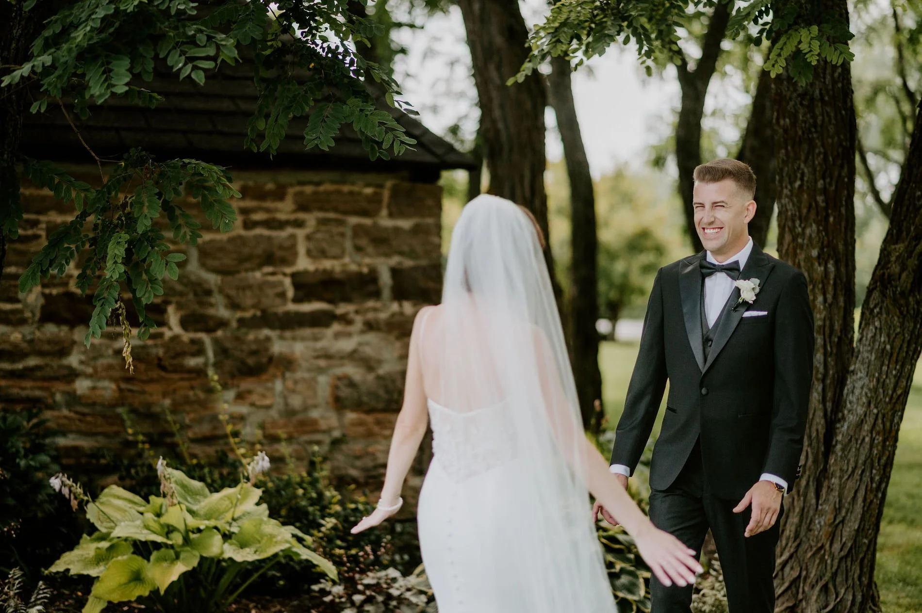 Austin grinning as he turns to see Emily for the first time under the trees at Stonefields Estate