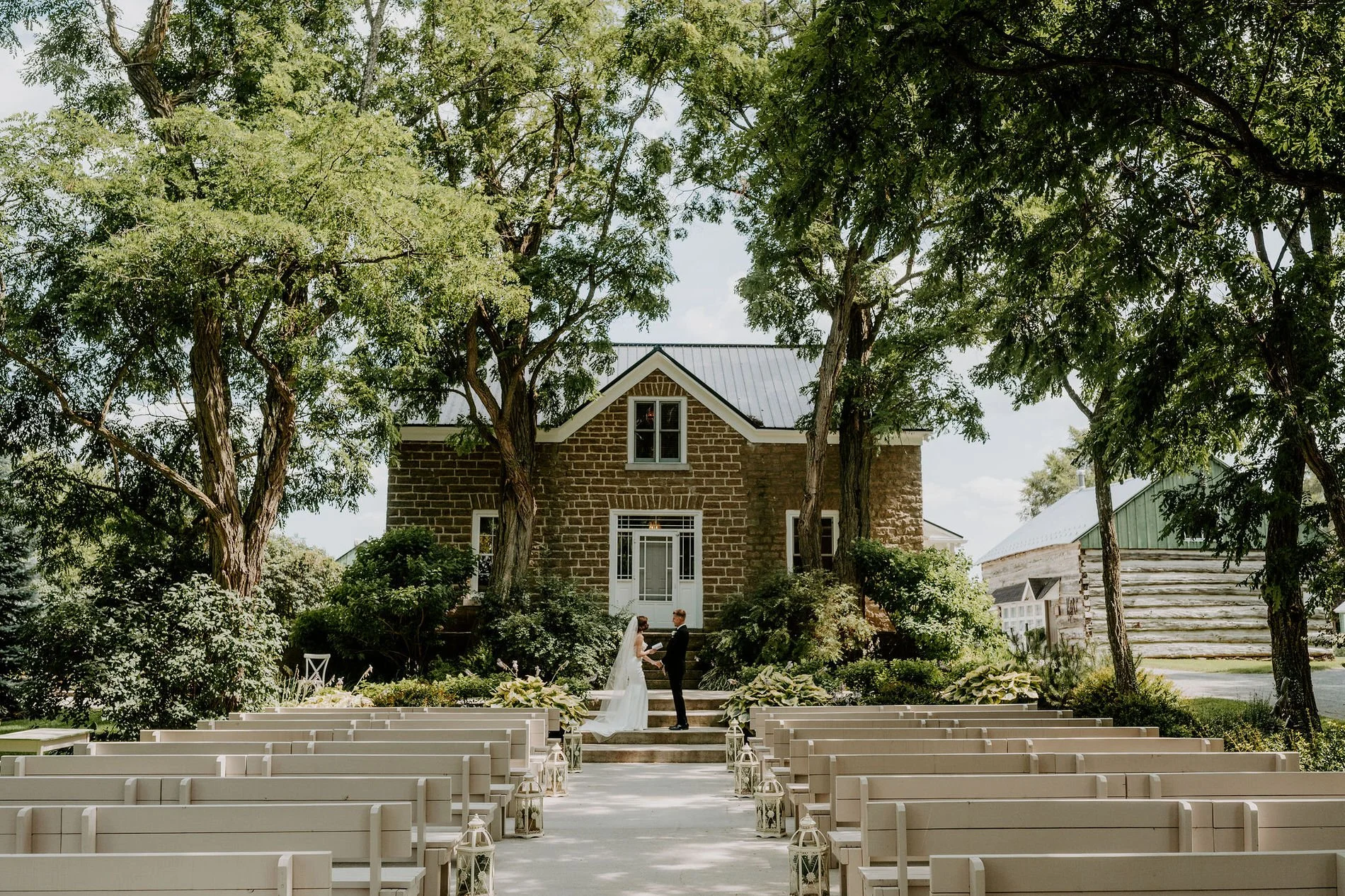 Emily and Austin on the steps of the historic stone house at Stonefields Estate, framed by rows of white benches