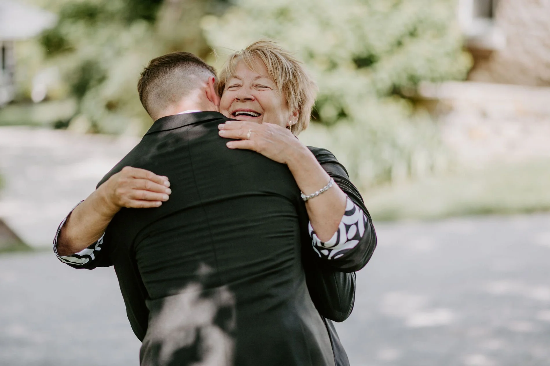 An older woman beaming as she hugs Austin before the ceremony