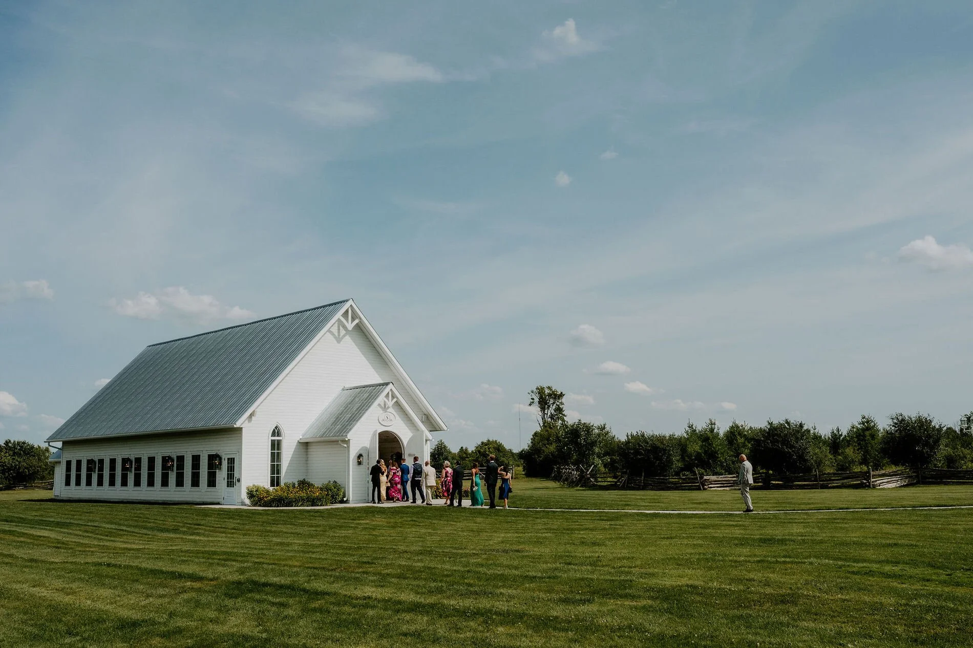 Guests gathering at the white chapel at Stonefields Estate under a wide summer sky