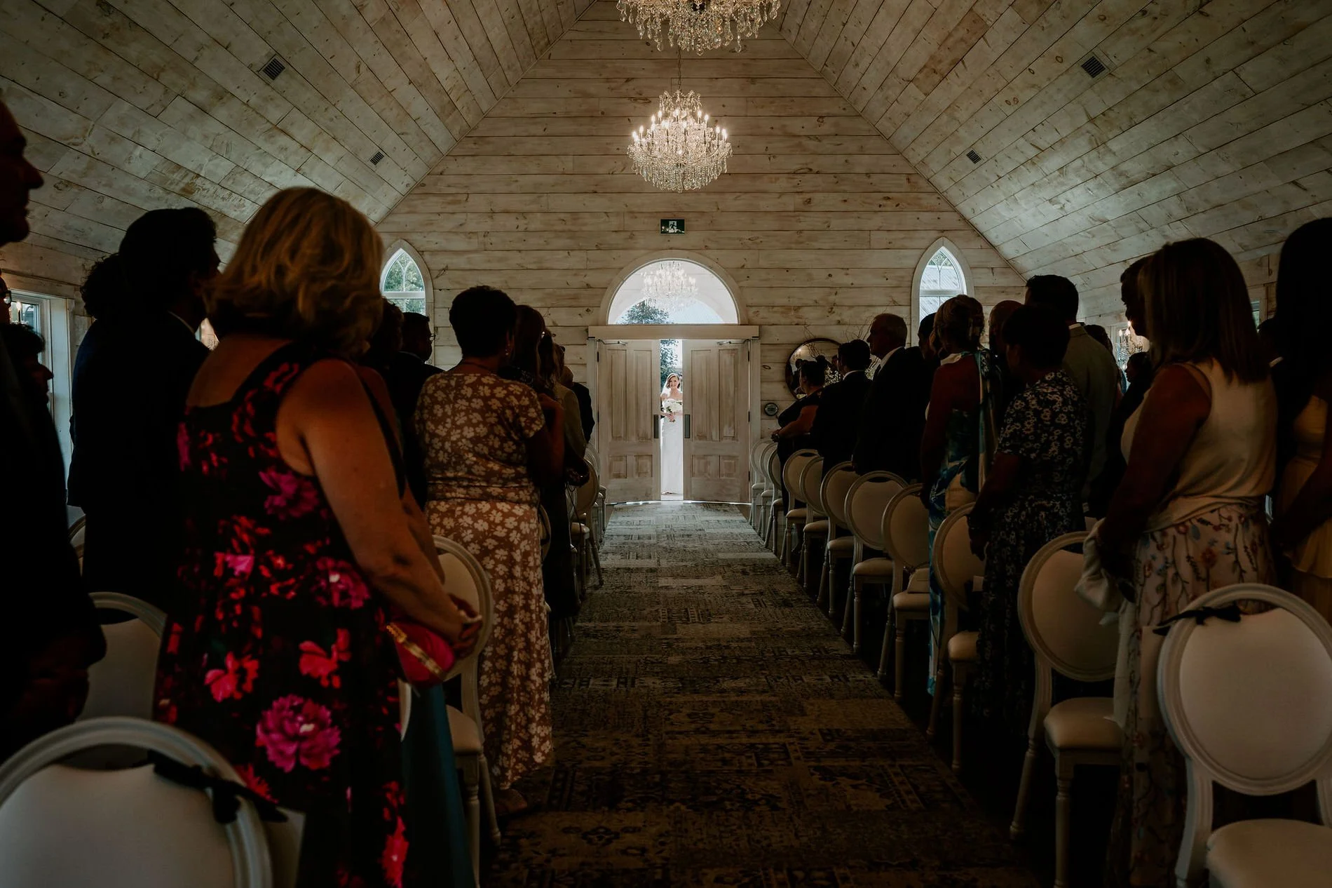 Guests standing in the chapel as Emily appears in the doorway at the end of the aisle