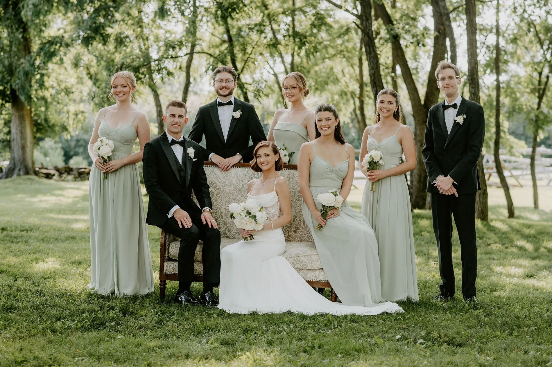 Emily and Austin's wedding party posed around a vintage settee on the lawn at Stonefields Estate