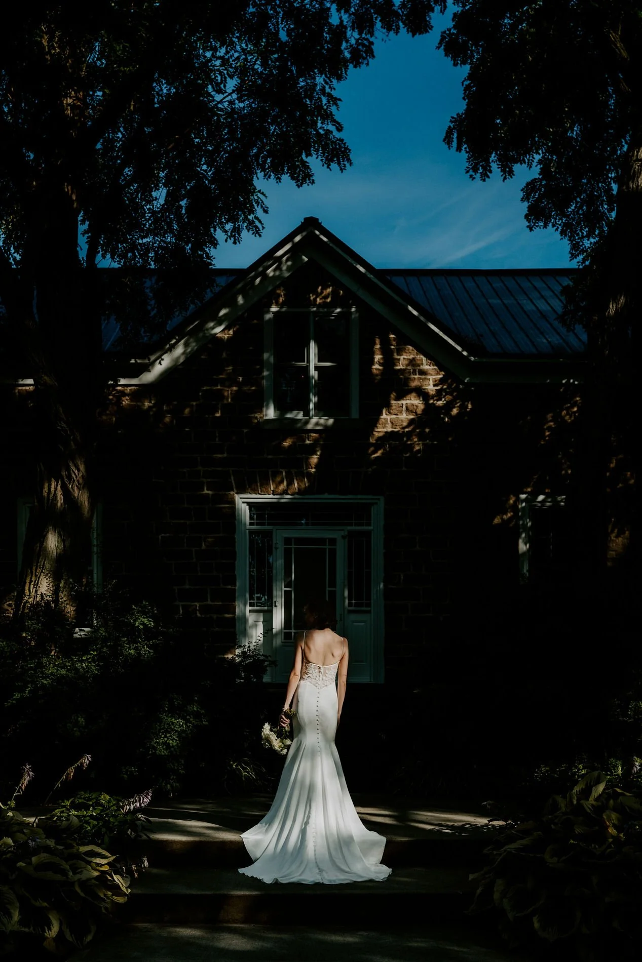 Emily seen from behind in dappled light, facing the stone house at Stonefields Estate