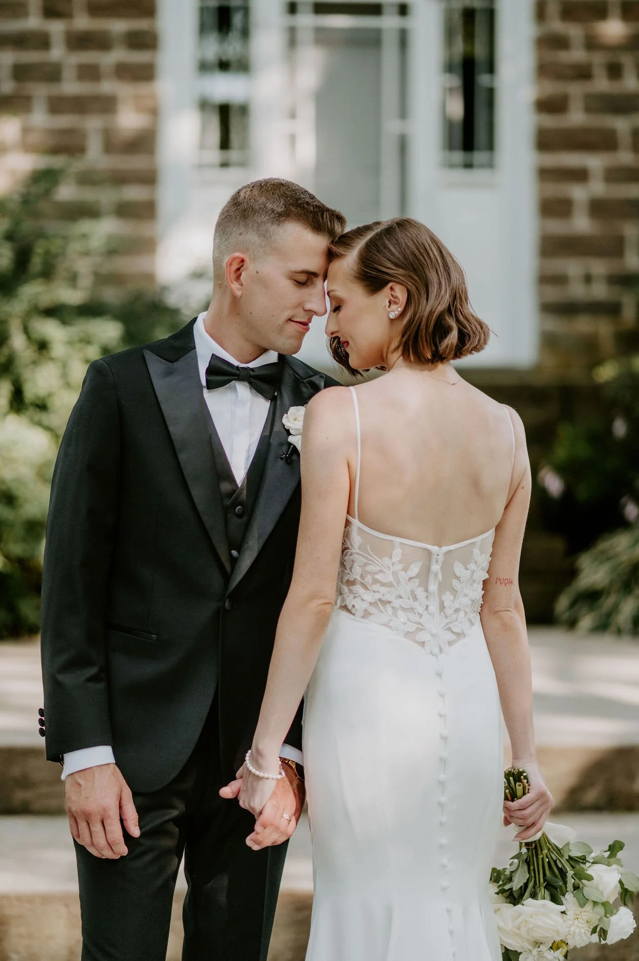 Emily and Austin forehead to forehead, holding hands in front of the stone house