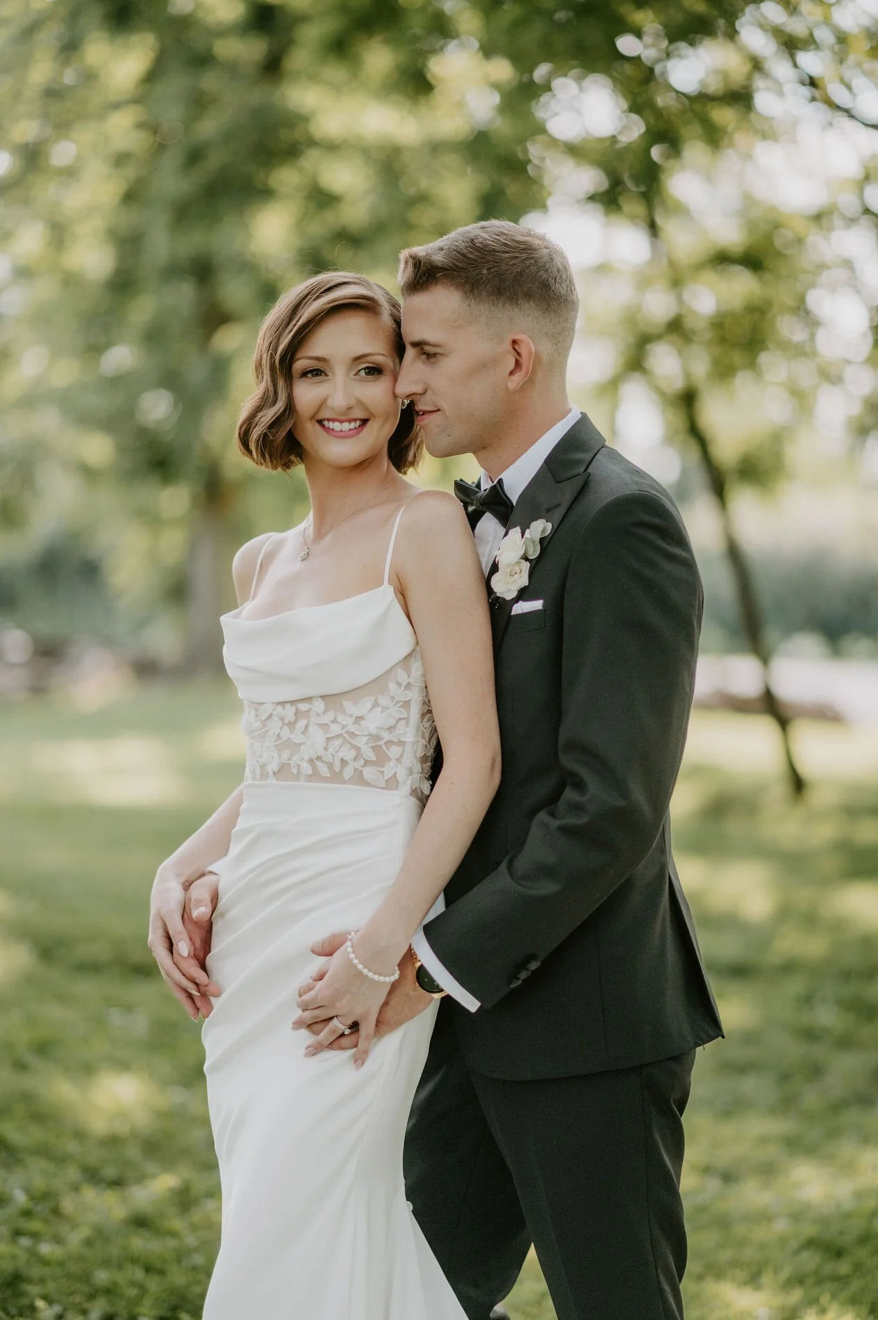 Emily smiling as Austin holds her close in the sunlit grounds of Stonefields Estate near Ottawa