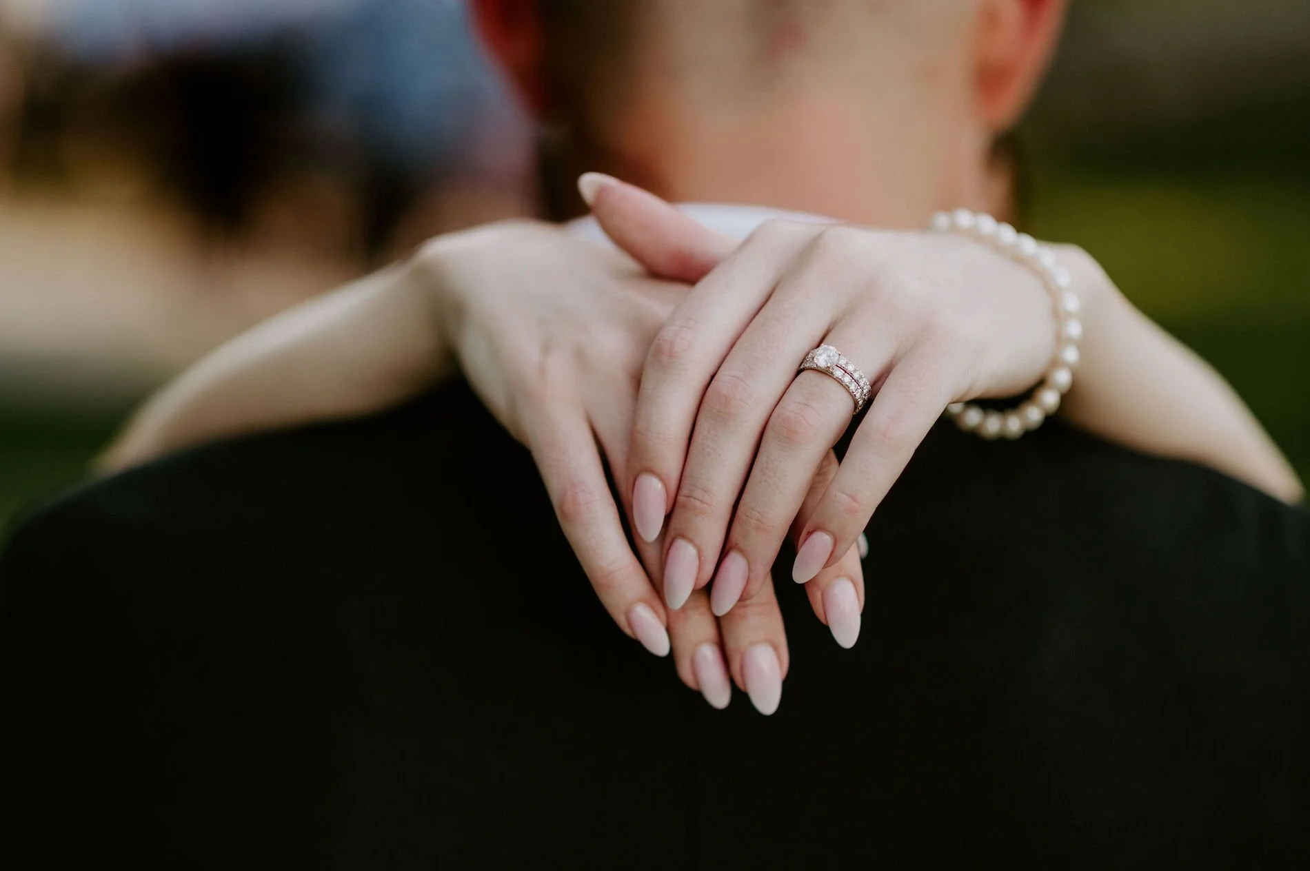 Close-up of Emily's engagement ring and pearl bracelet as her hands rest on Austin's shoulder