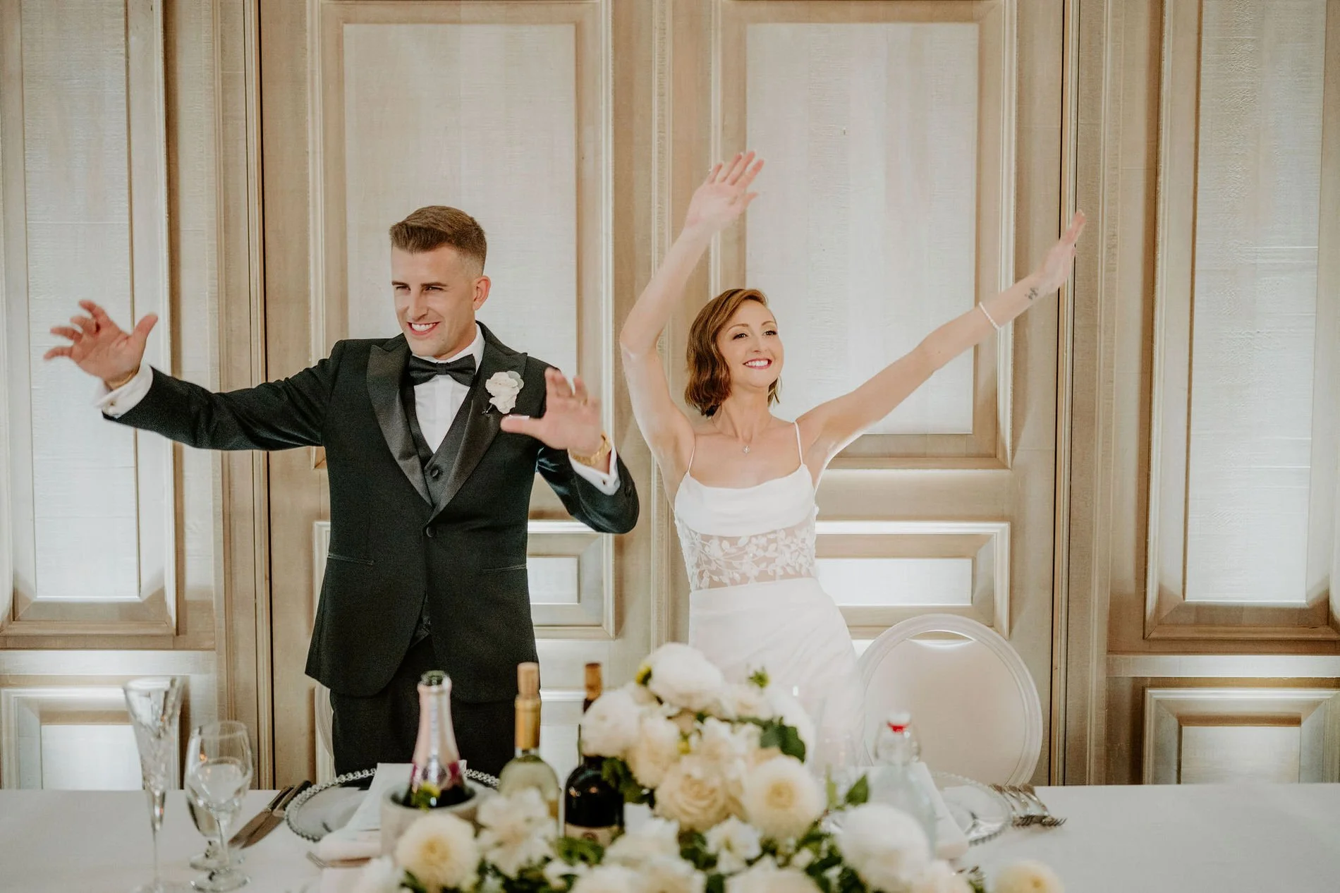 Emily and Austin throwing their arms up in celebration at the head table