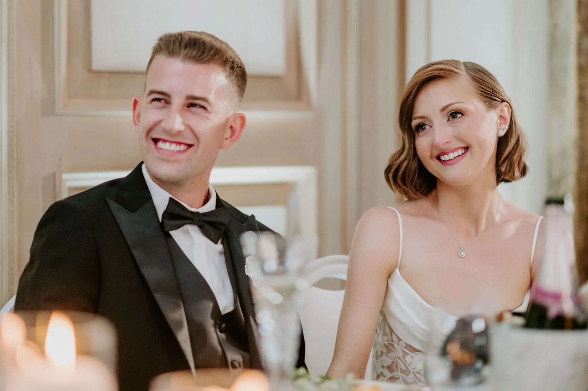 Emily and Austin smiling at the candlelit head table during the speeches