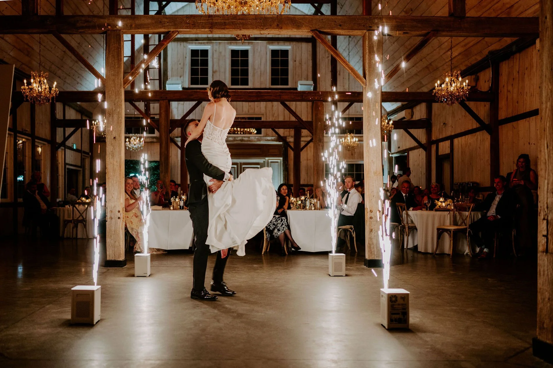 Austin lifting Emily during their first dance as sparkler fountains light up the barn at Stonefields Estate