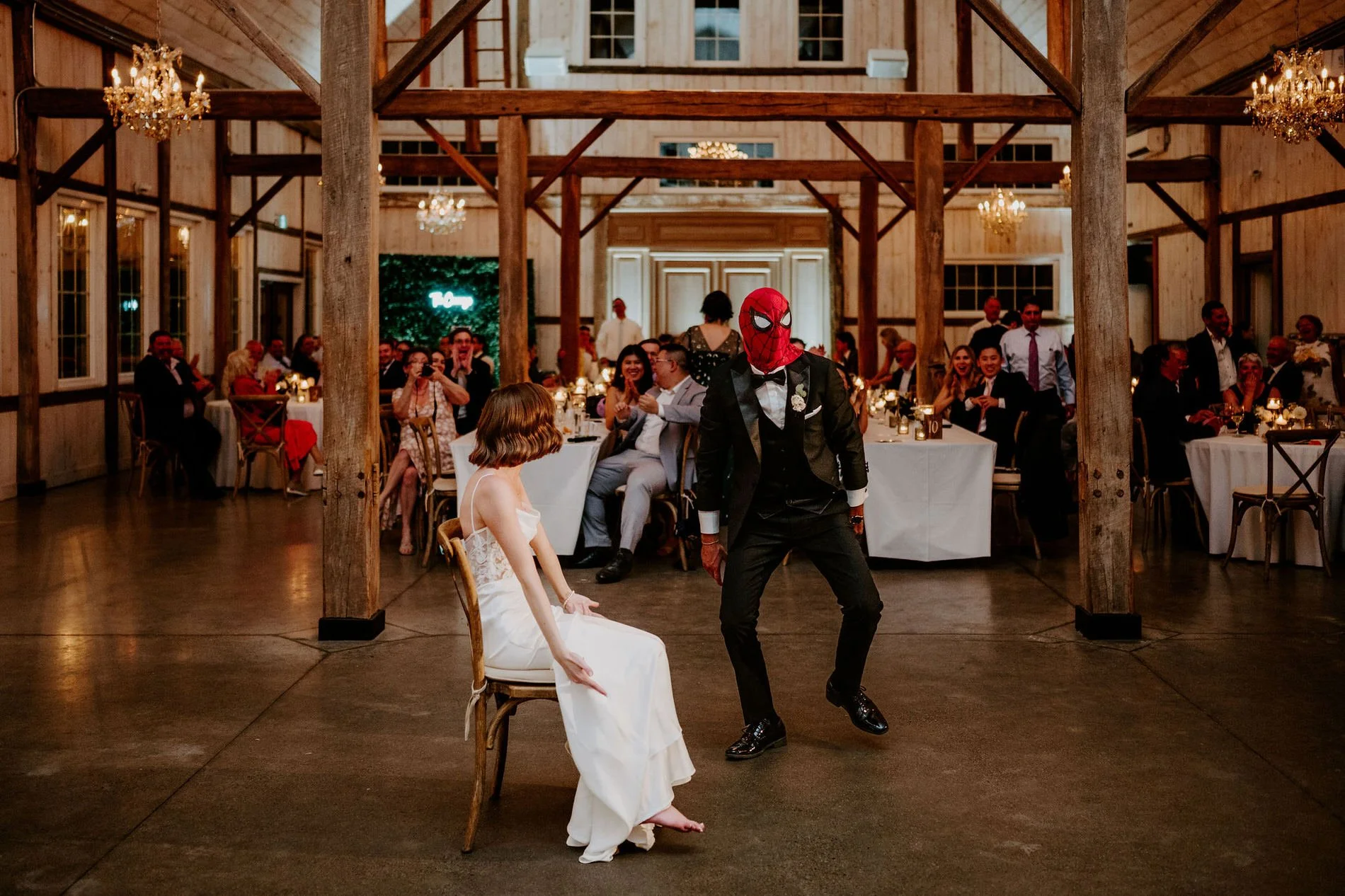 Austin dancing in a Spider-Man mask as Emily watches from a chair in the middle of the dance floor
