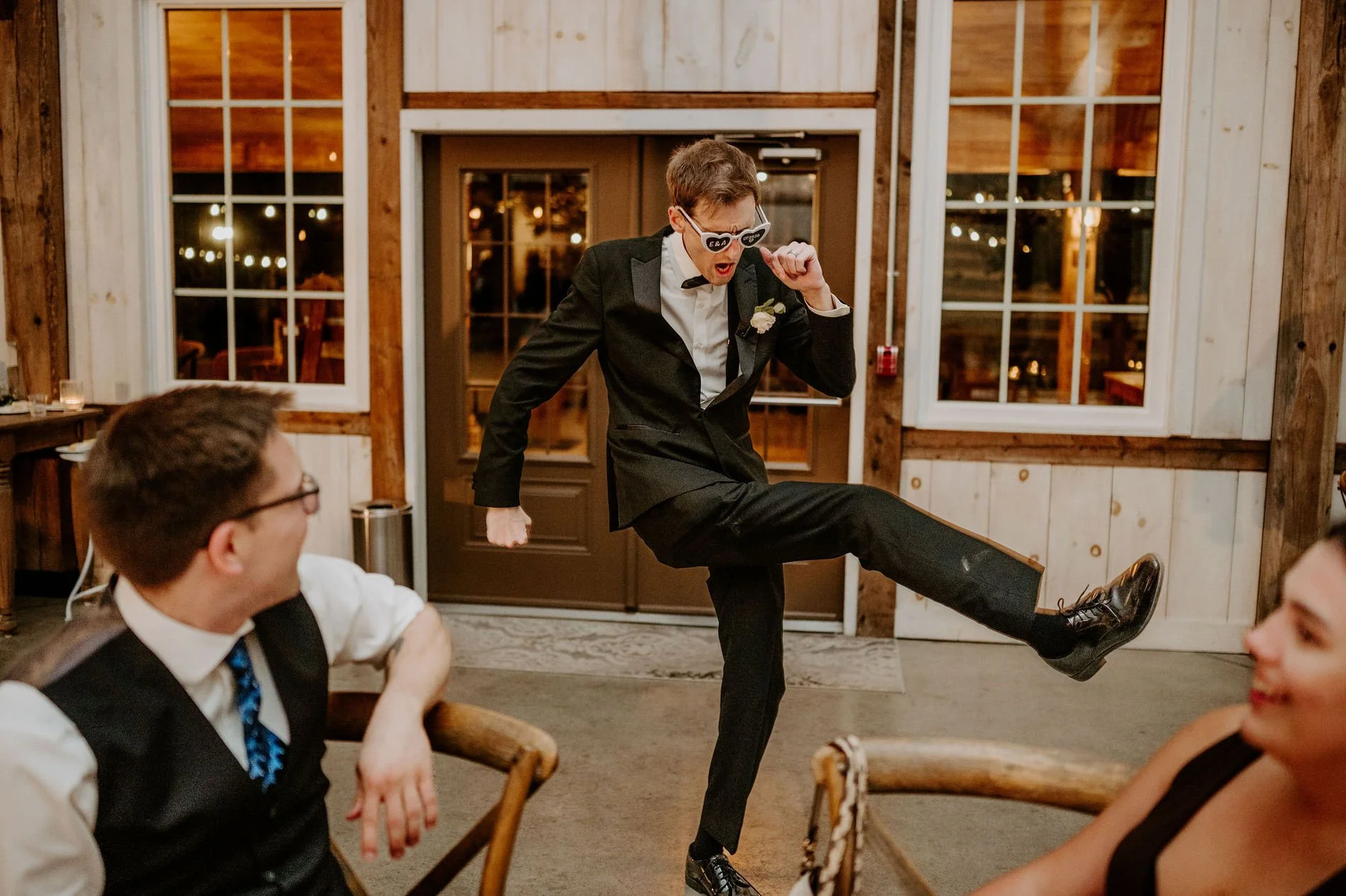 A groomsman in sunglasses doing a high kick on the dance floor