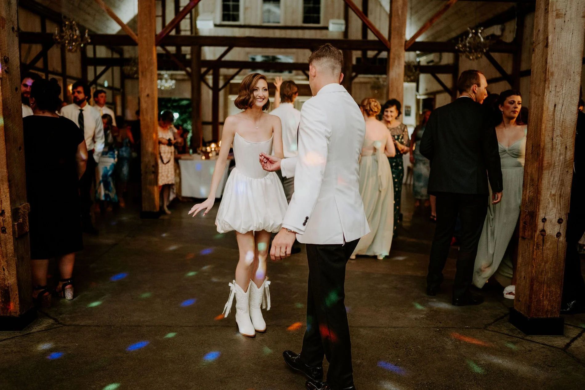 Emily in white cowboy boots dancing with Austin under disco lights in the Stonefields barn