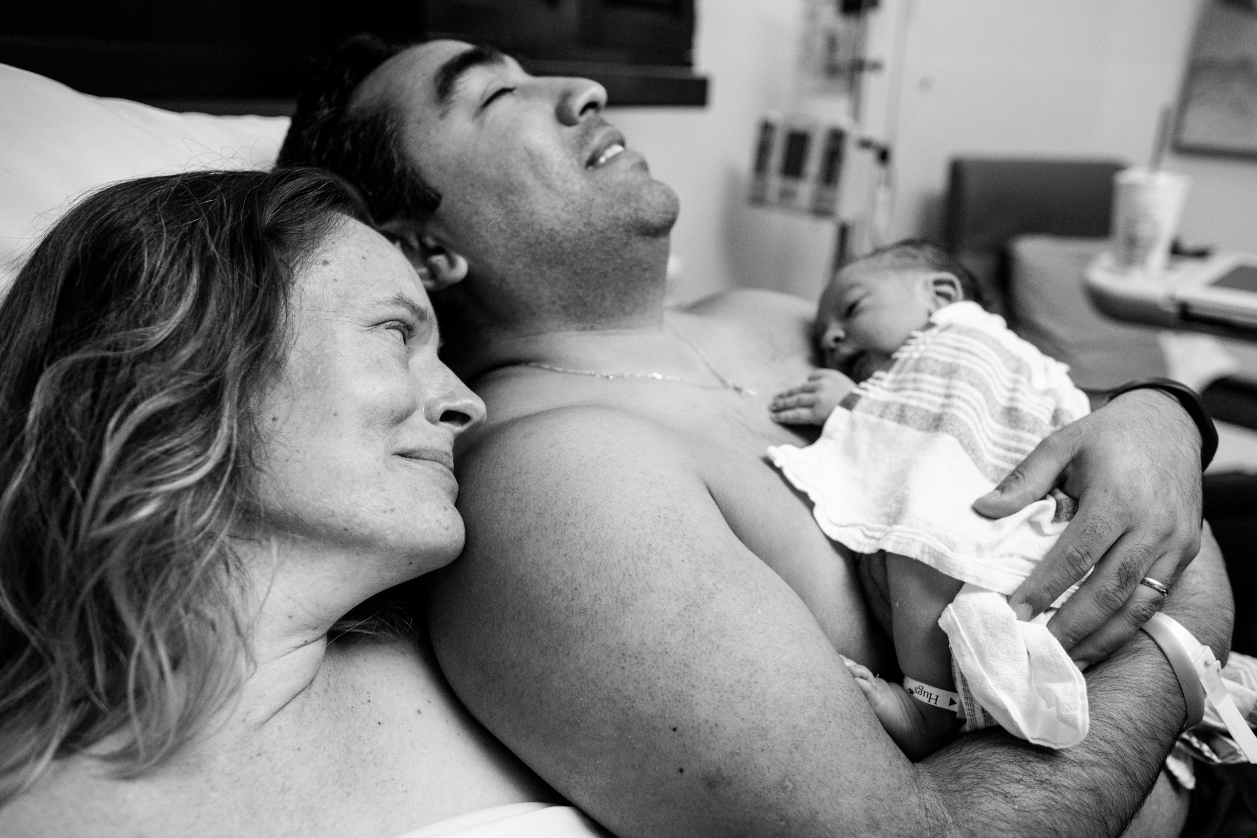 new mom looking lovingly at newborn baby resting on dad's chest