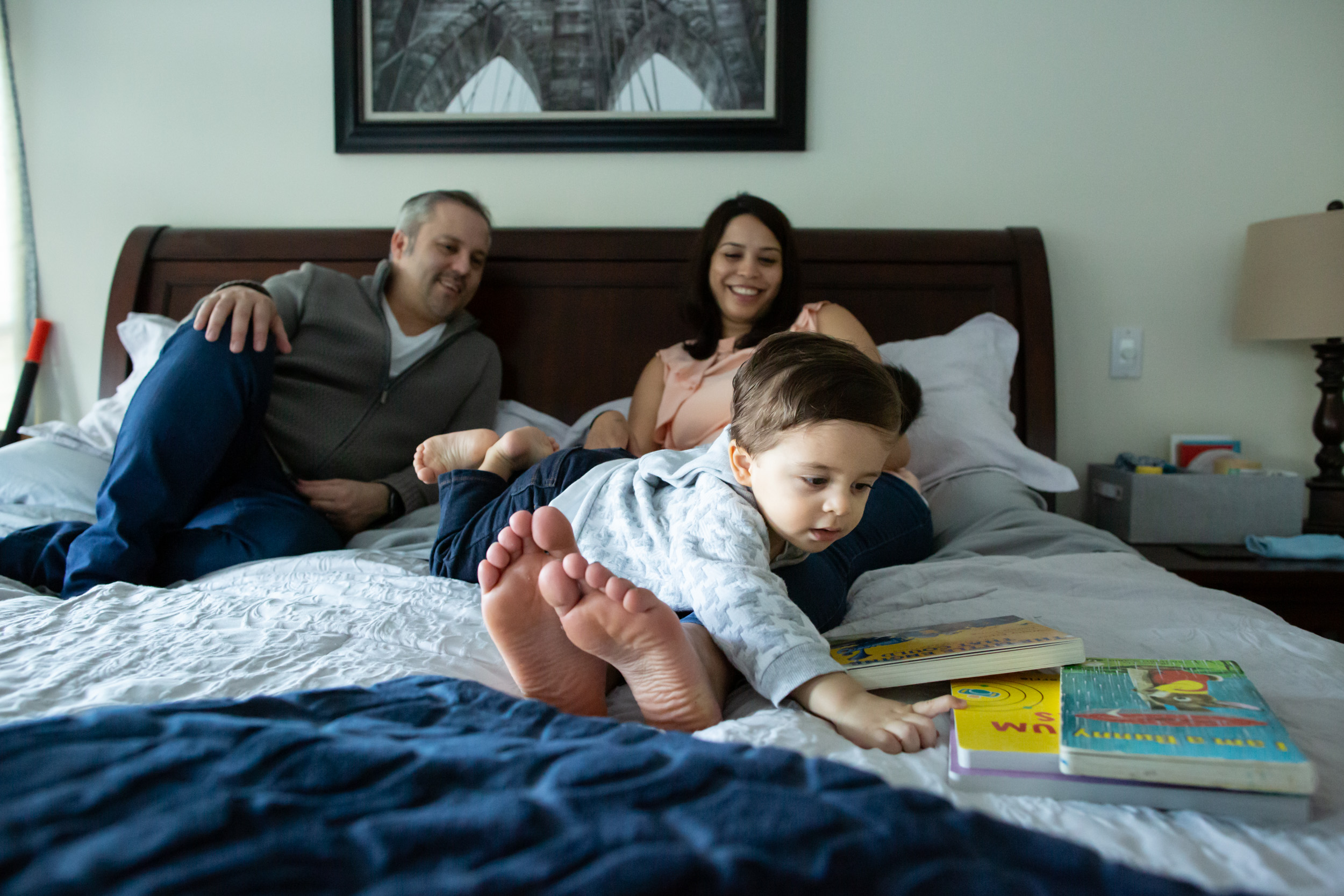 family on a bed with child reaching for book to read