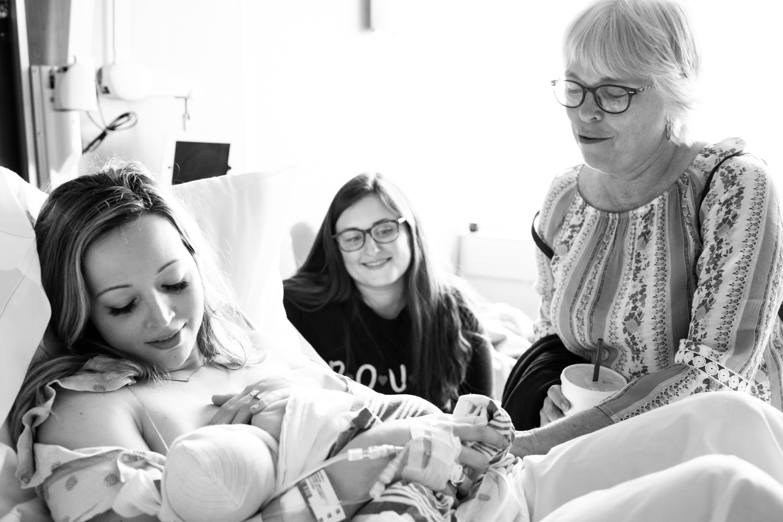 grandmother and doula looking on as new mom breastfeeds