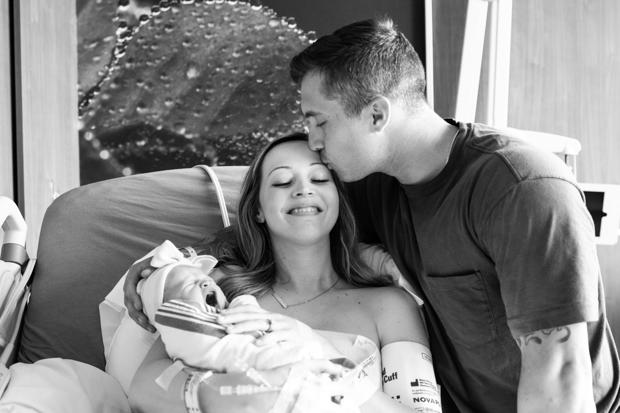 new dad kissing his wife while holding newborn baby girl