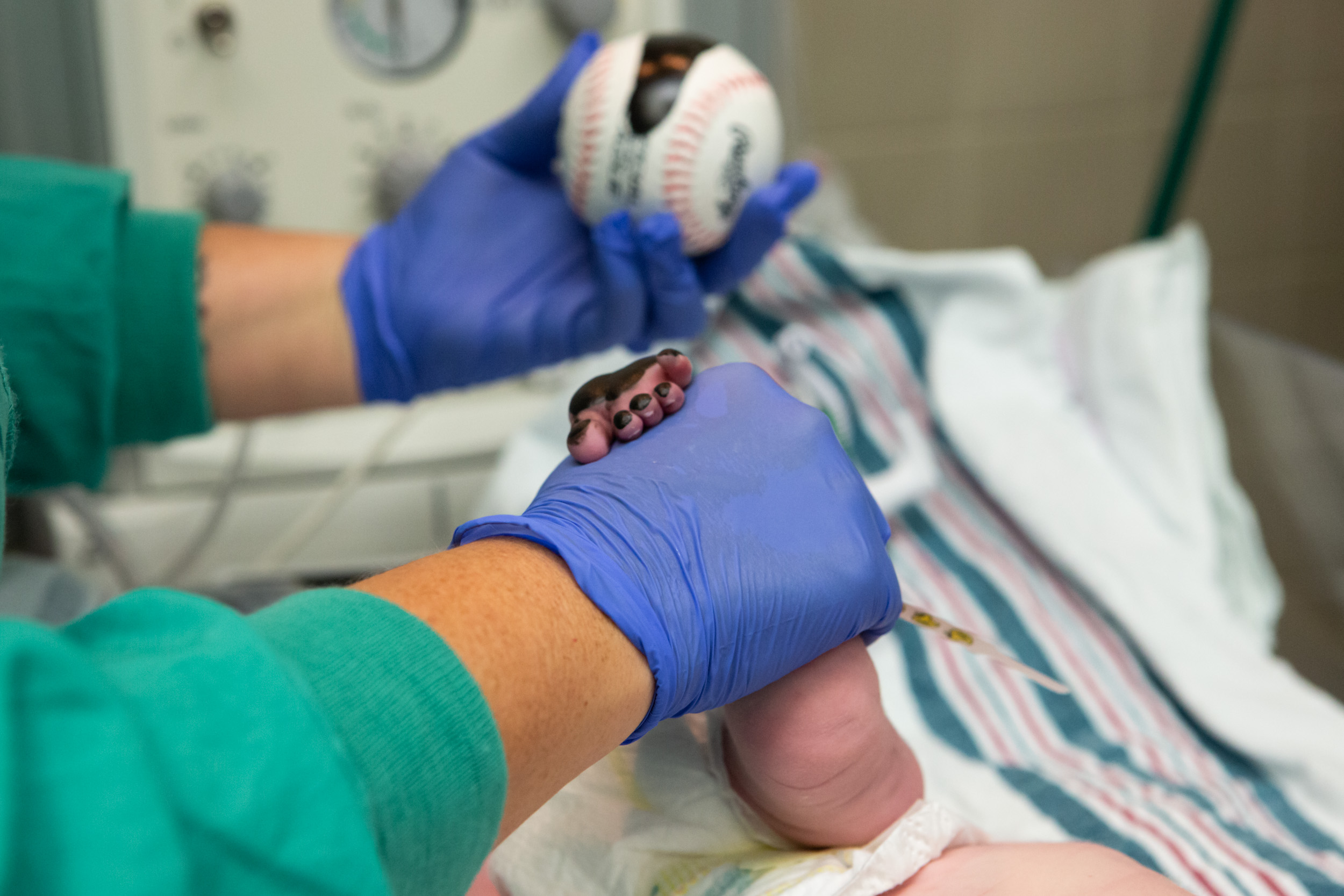 newborn baby boy getting footprint stamped on baseball